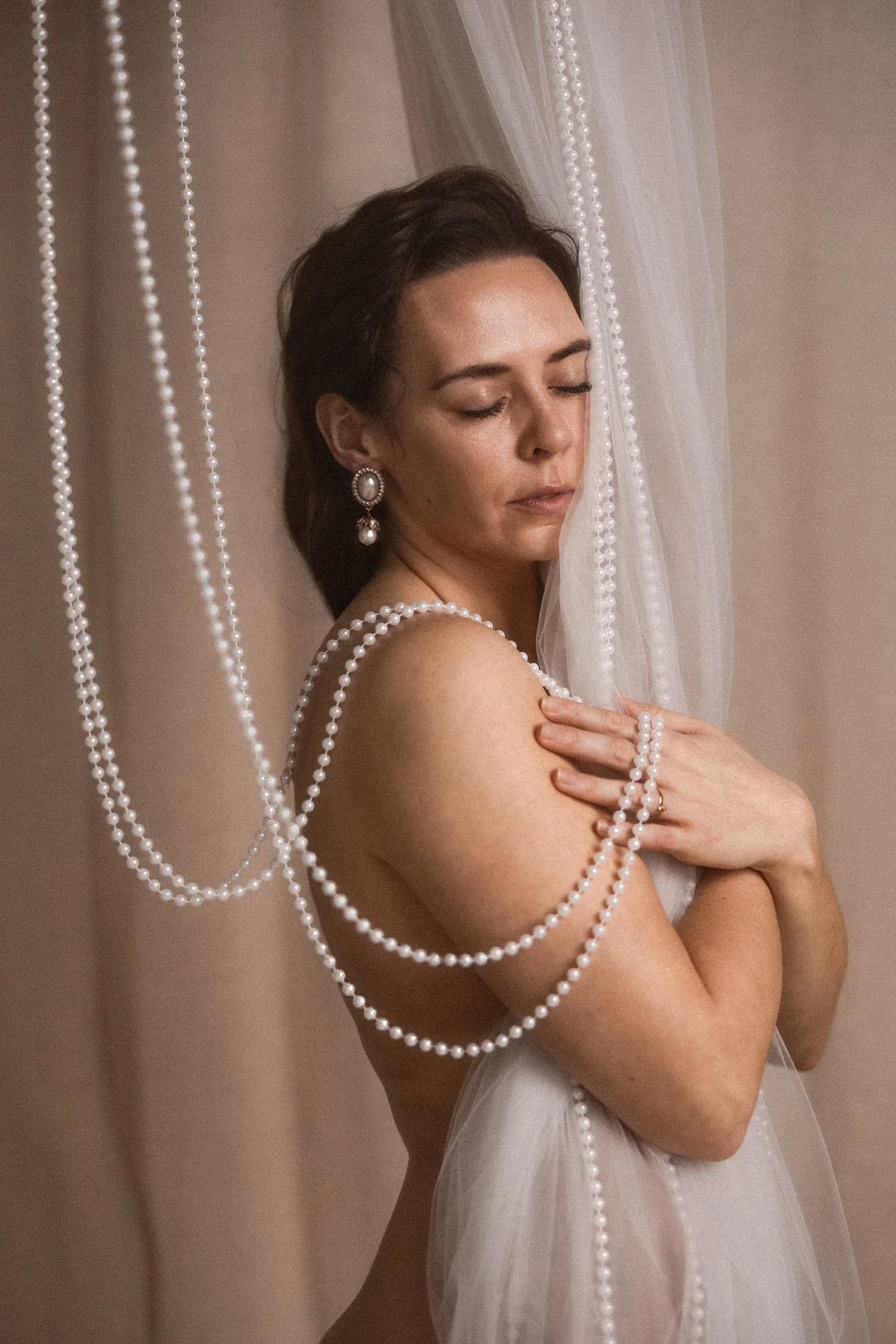 Buduarowa fotografia kobiety w klimacie filmowym z koralami i tiulami. W tle beżowe minimalistyczne tło.