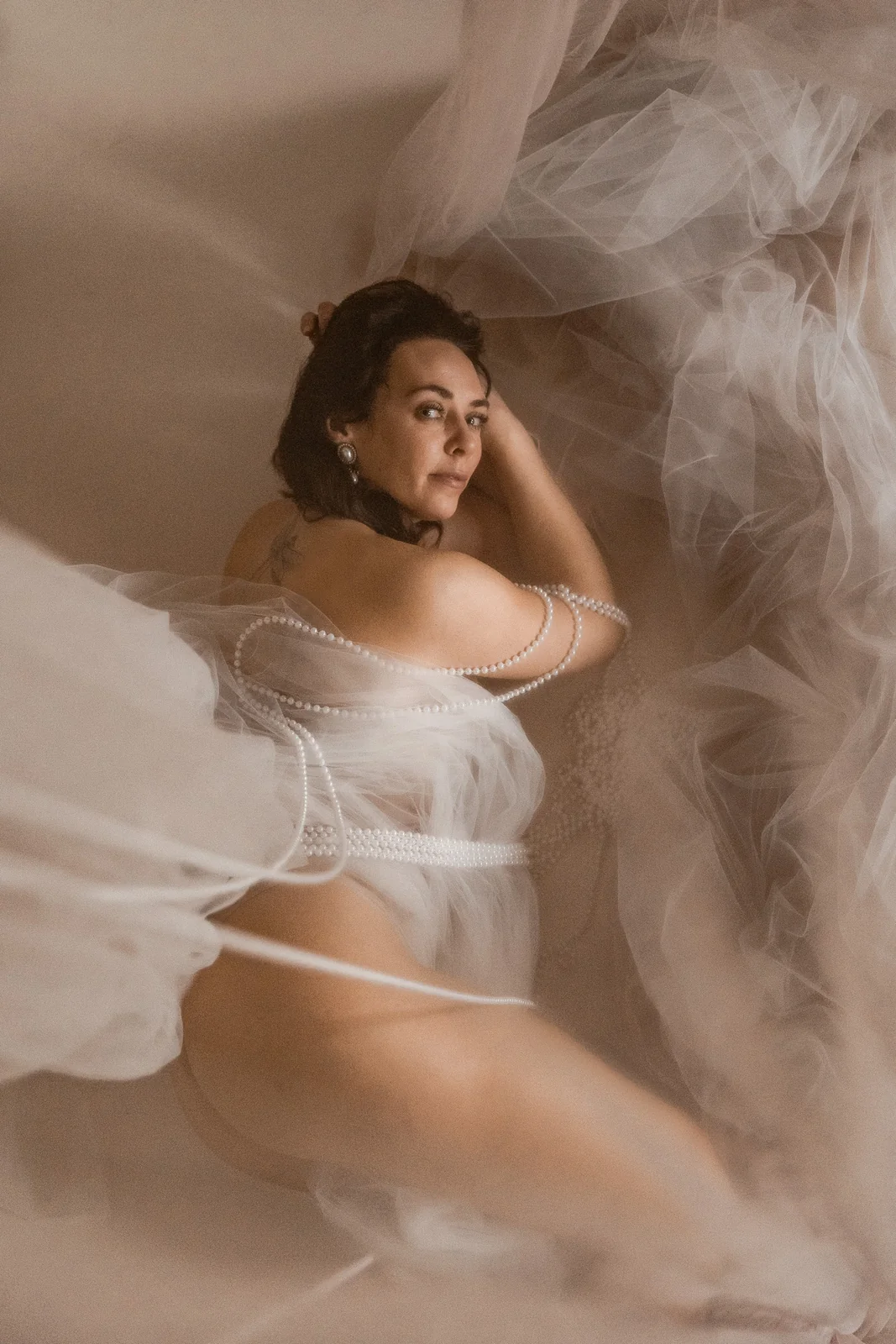 Sensualny portret kobiecy w studio. Kobieta otulona delikatnym materiałem i koralami.