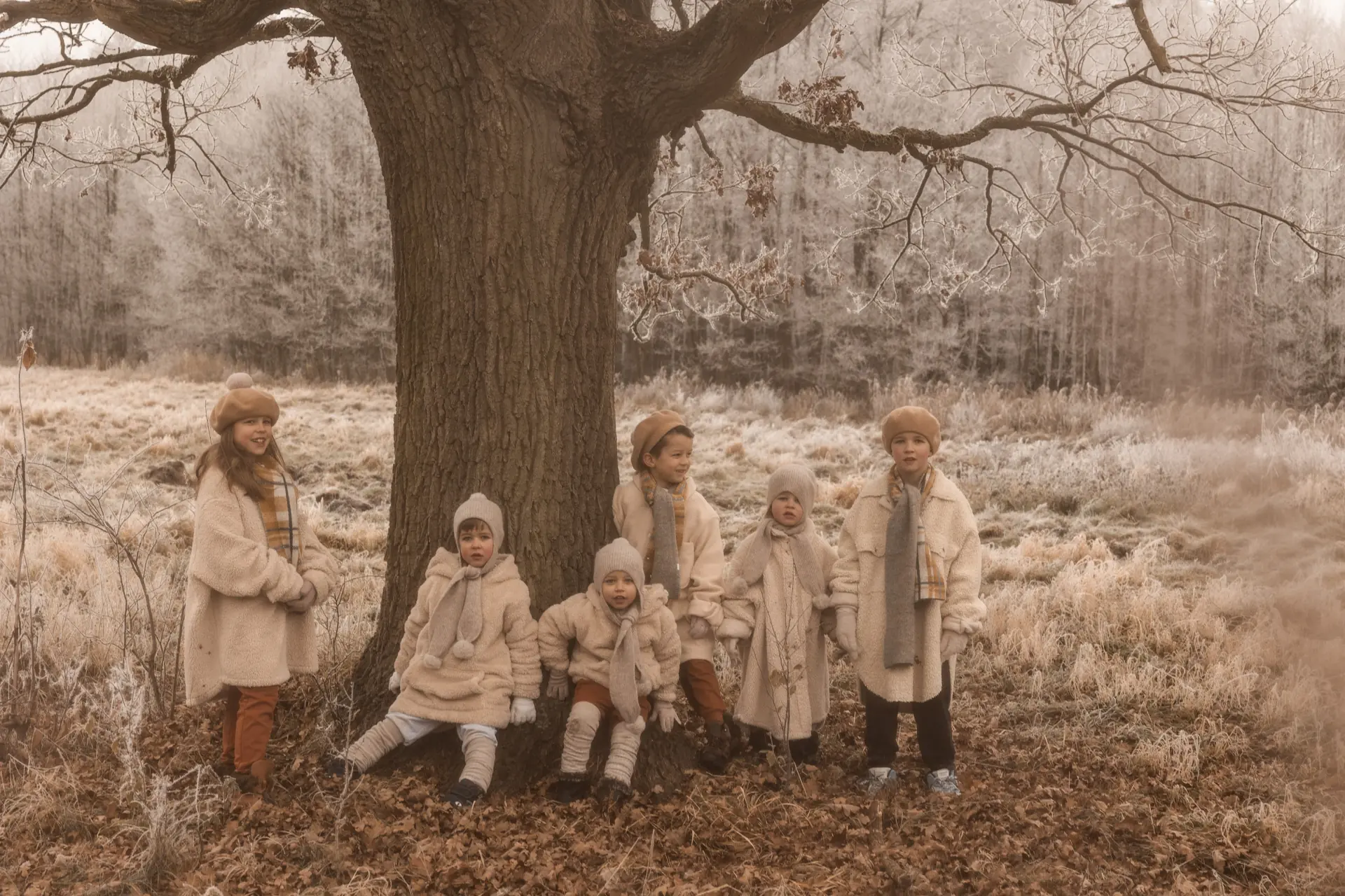Szóstka dzieci ubrane w retro ubrania stojąca obok wielkiego drzewa podczas zimowej sesji zdjęciowej w plenerze