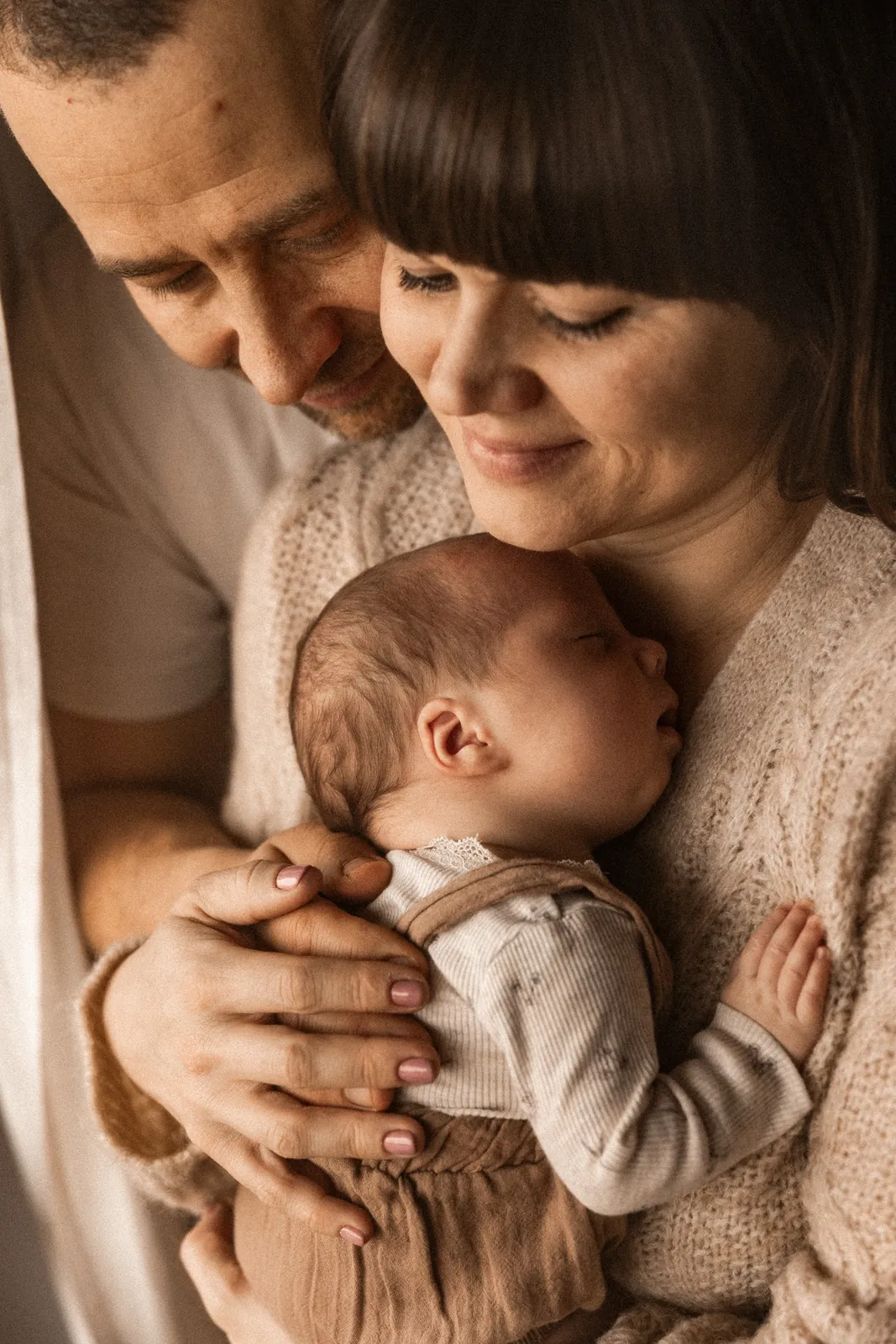 Rodzice czule przytulają śpiącego noworodka podczas naturalnej sesji noworodkowej w domu