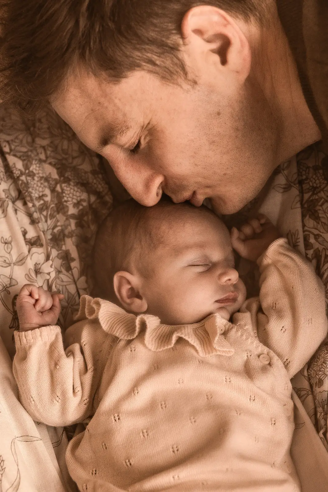 Tata całujący główkę śpiącego dziecka podczas sesji noworodkowej w studiu