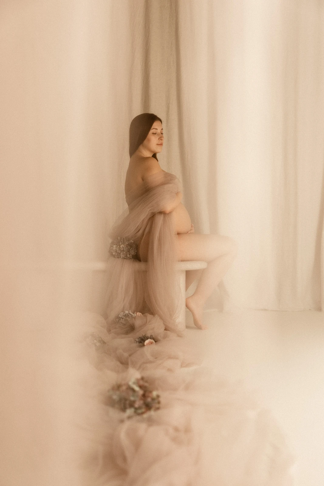 Sensualny portret przyszłej mamy delikatnie otulającej rękami brzuszek podczas sesji ciążowej w studiu w Poznaniu