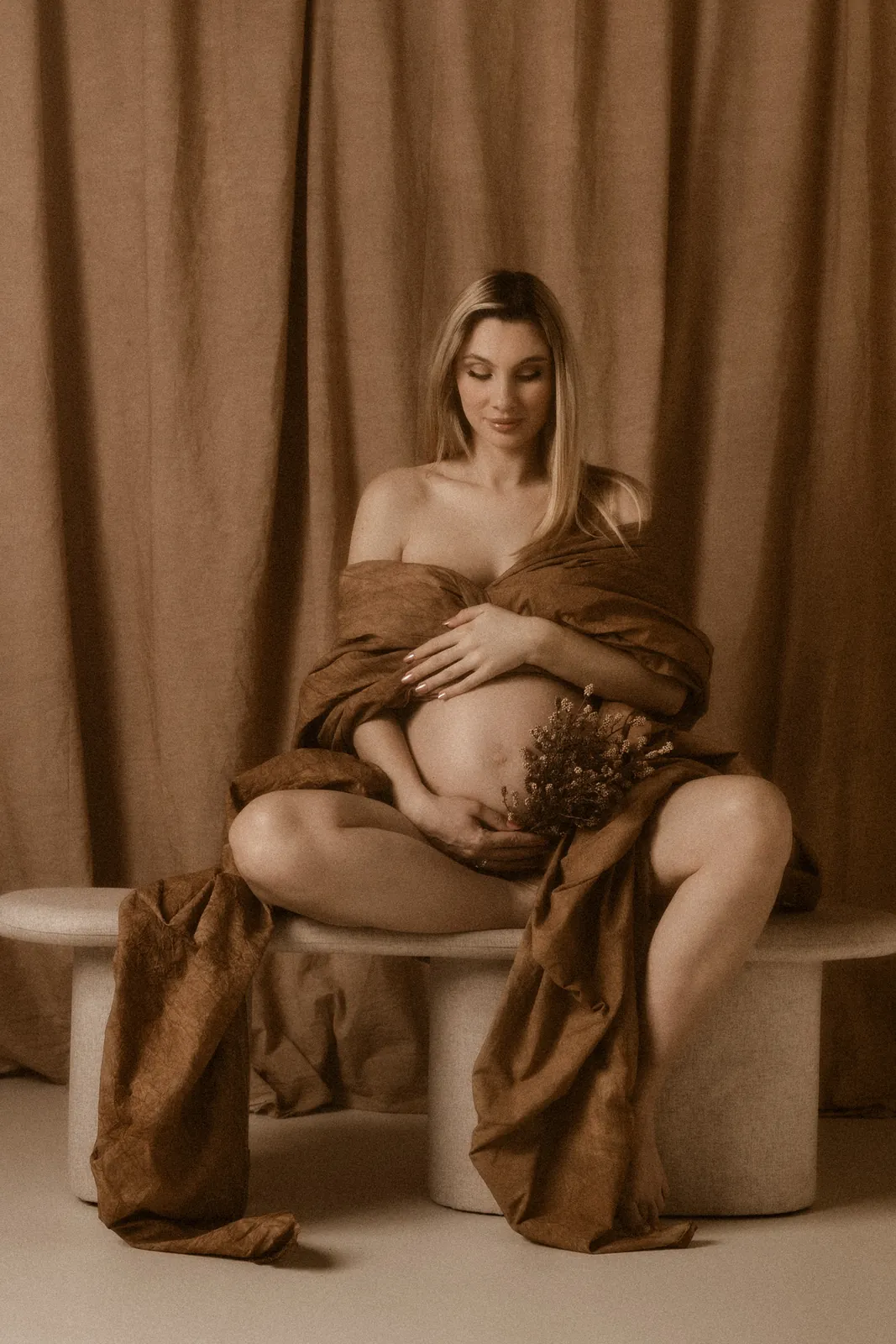 Kobieta w ciąży w eterycznej stylizacji z kwiatem podczas minimalistycznej sesji w studiu