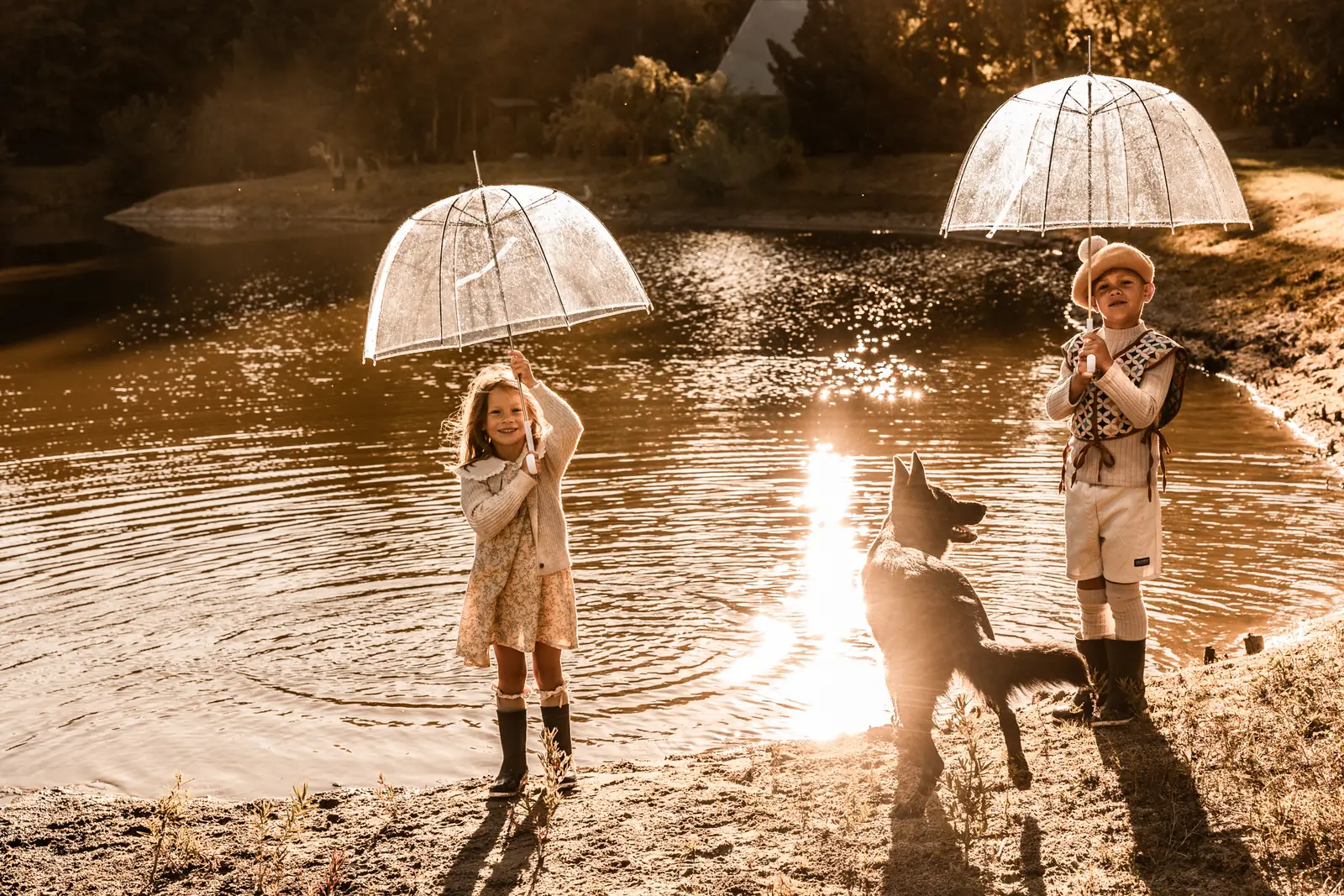 Dzieci bawiące się nad wodą z parasolami w towarzystwie ich psa towarzysza podczas lifestylowej sesji zdjęciowej