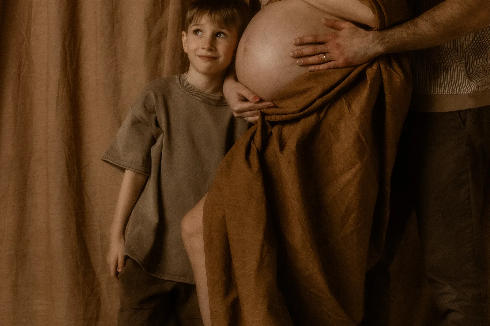 Rodzinna sesja ciążowa w studiu z partnerem i dzieckiem przytulającym twarzą brzuch mamy