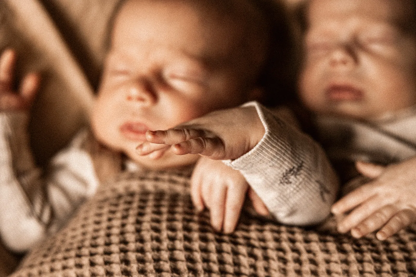 Dwójka maleńkich noworodków przytulona podczas spokojnego snu na jasnym kocyku