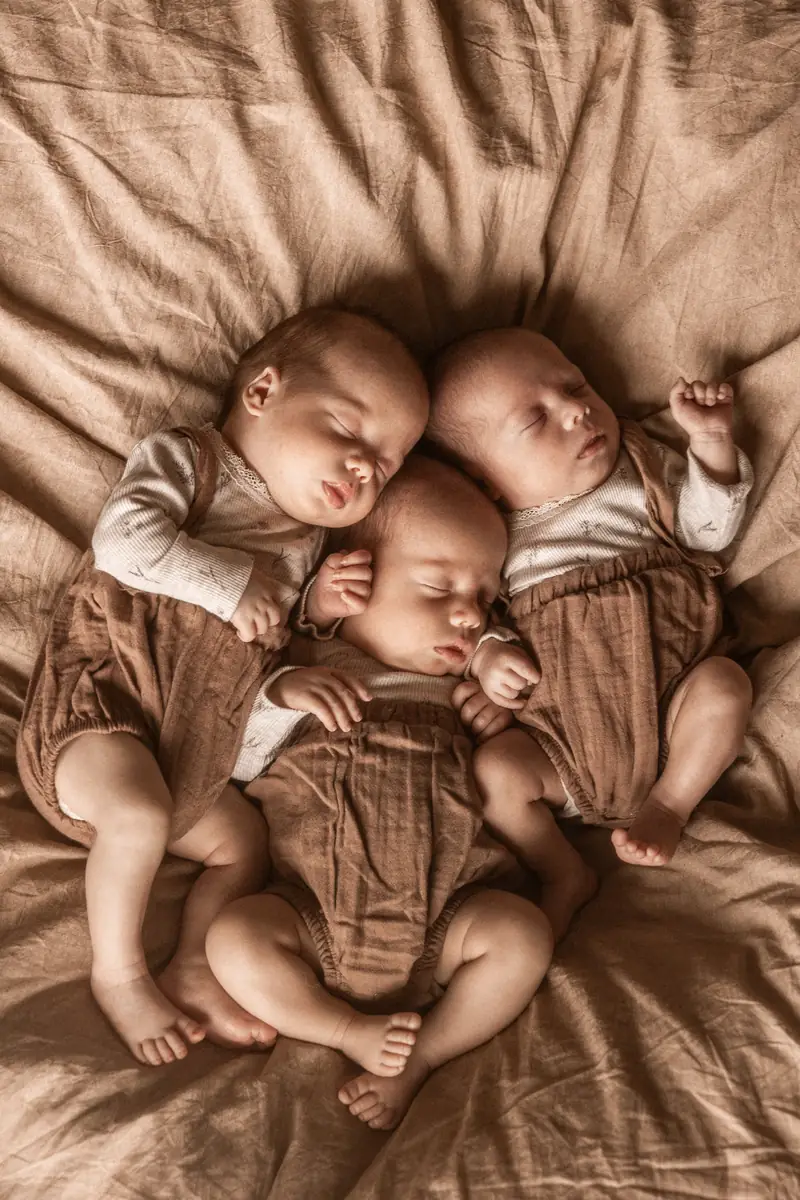 Zdjęcie trojaczków - trzy noworodki siostry śpiące na kocyku podczas sesji noworodkowej w domu