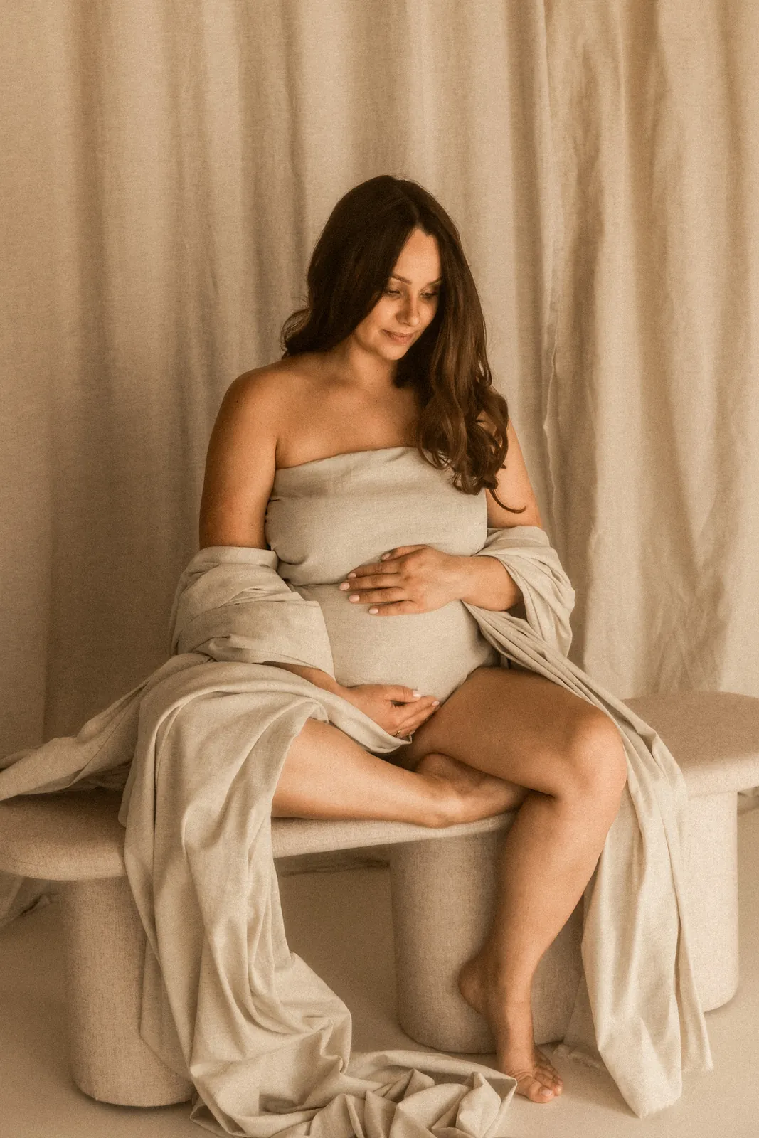 Subtelna fotografia przyszłej mamy - kobieta ubrana w jasny materiał delikatnie dotyka swój brzuszek