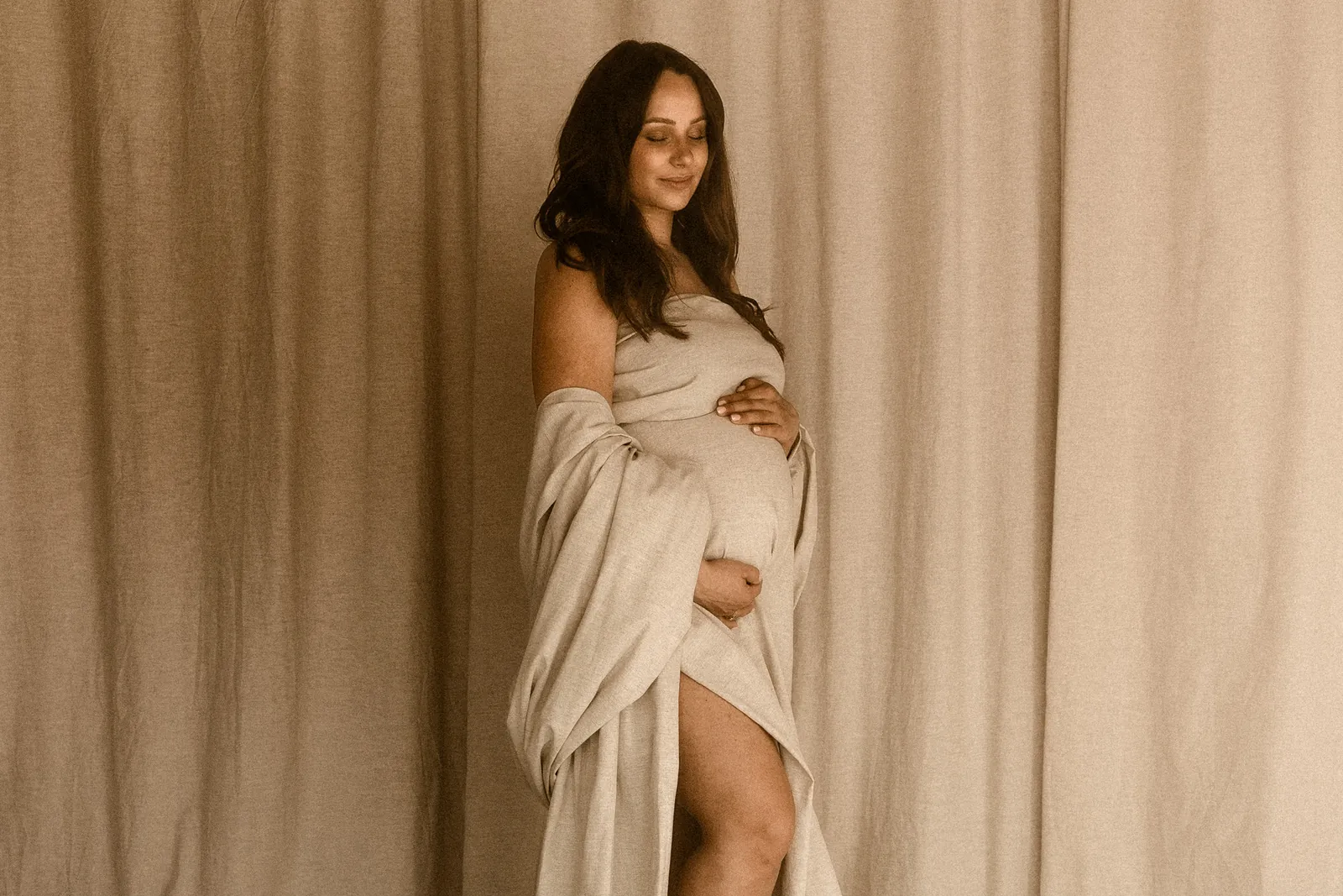 Ujęcie kobiety w ciąży z delikatnym uśmiechem podczas pozowania na sesji brzuszkowej