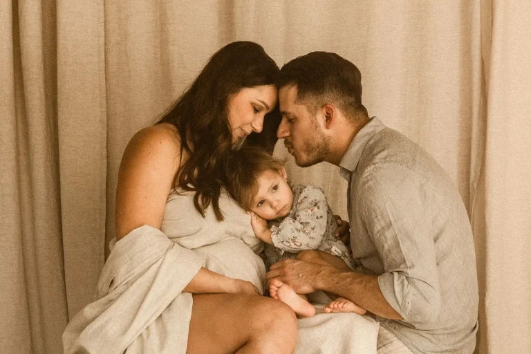 Dziecko siedzi na kolanach taty i przytula się do brzuszka mamy podczas sesji ciążowej w studiu