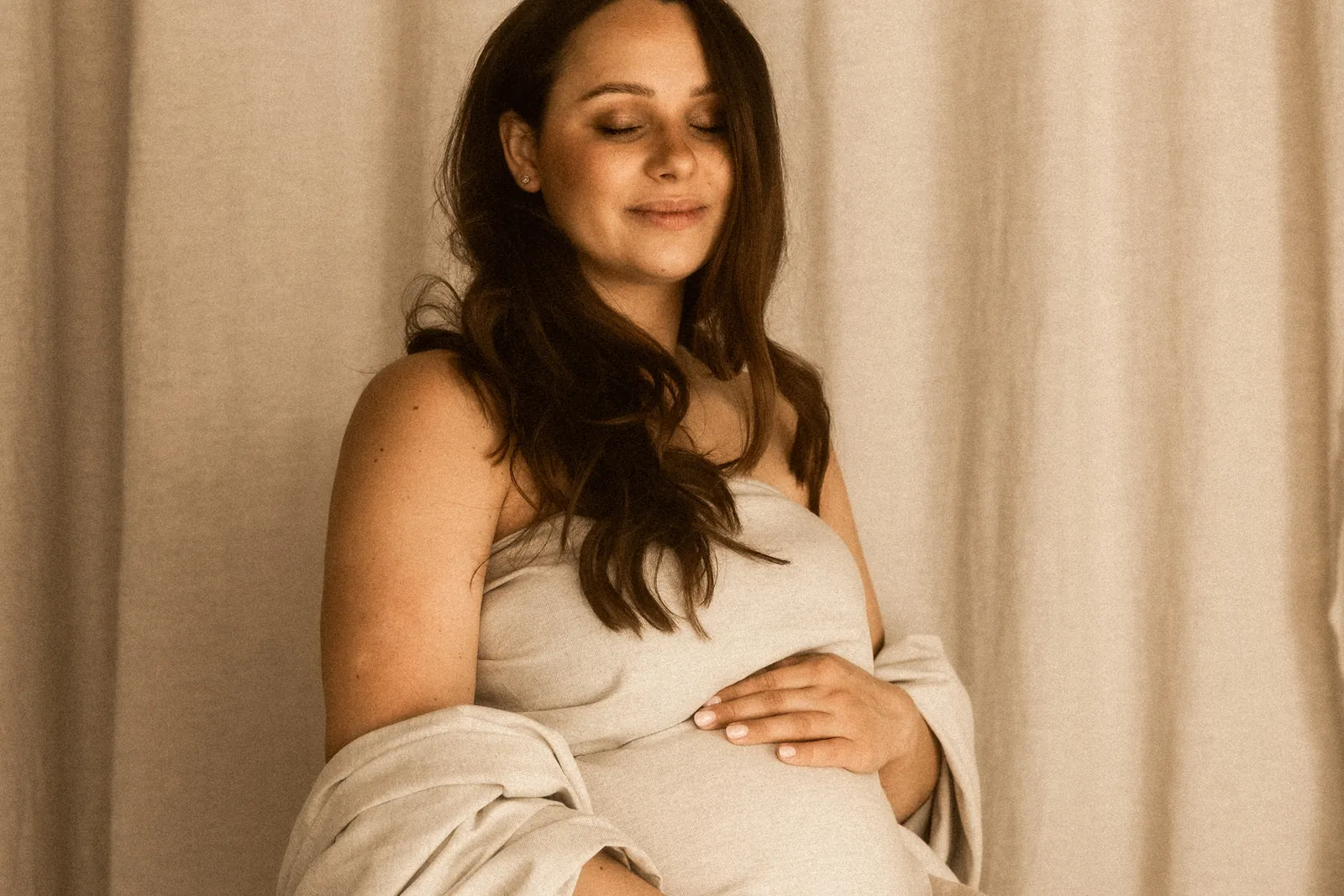 Sensualny portret przyszłej mamy w ciemnych włosach i jasnej sukni