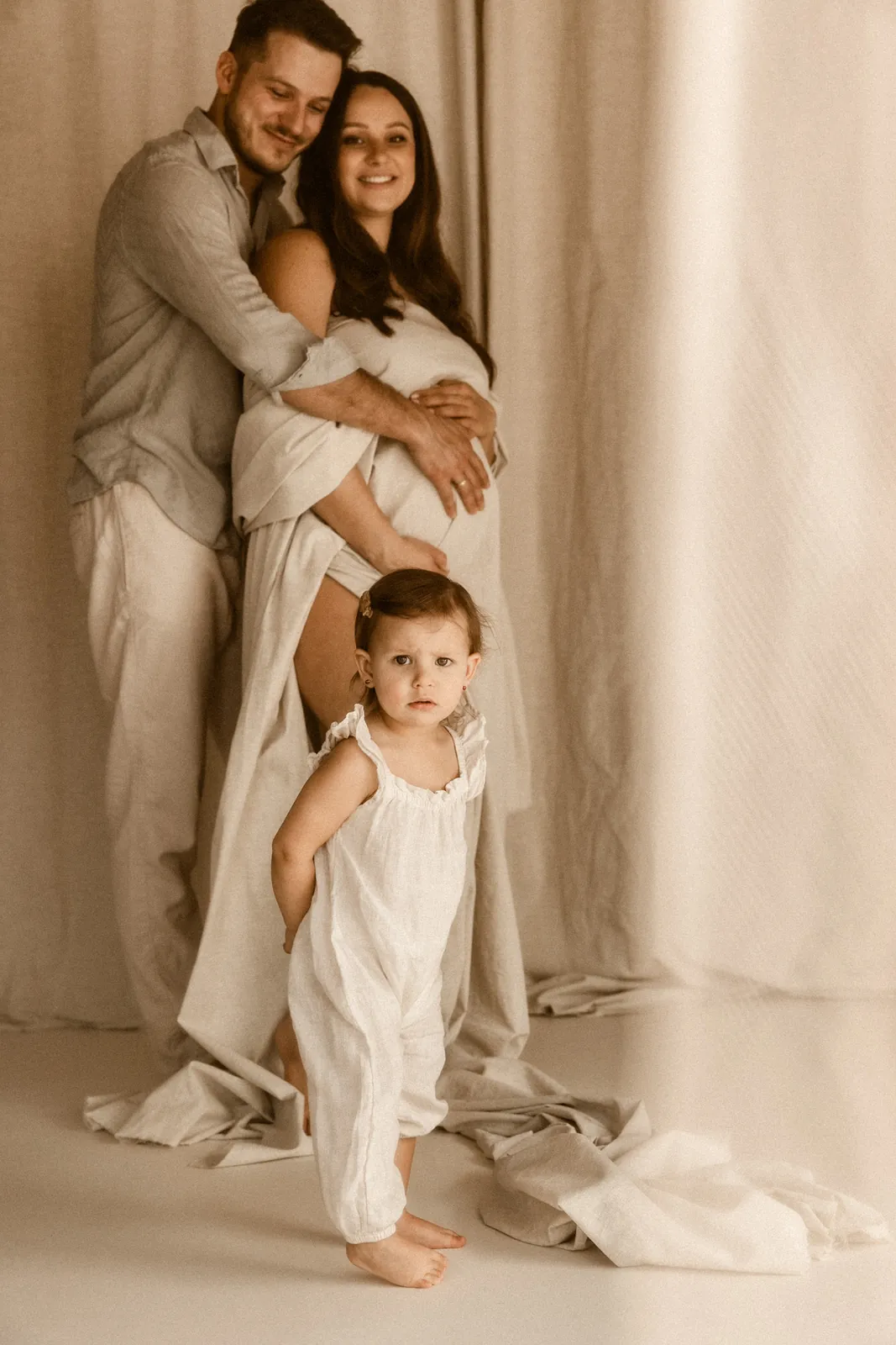 Rodzinna sesja ciążowa w studiu z partnerem i córką, rodzice przytulają się