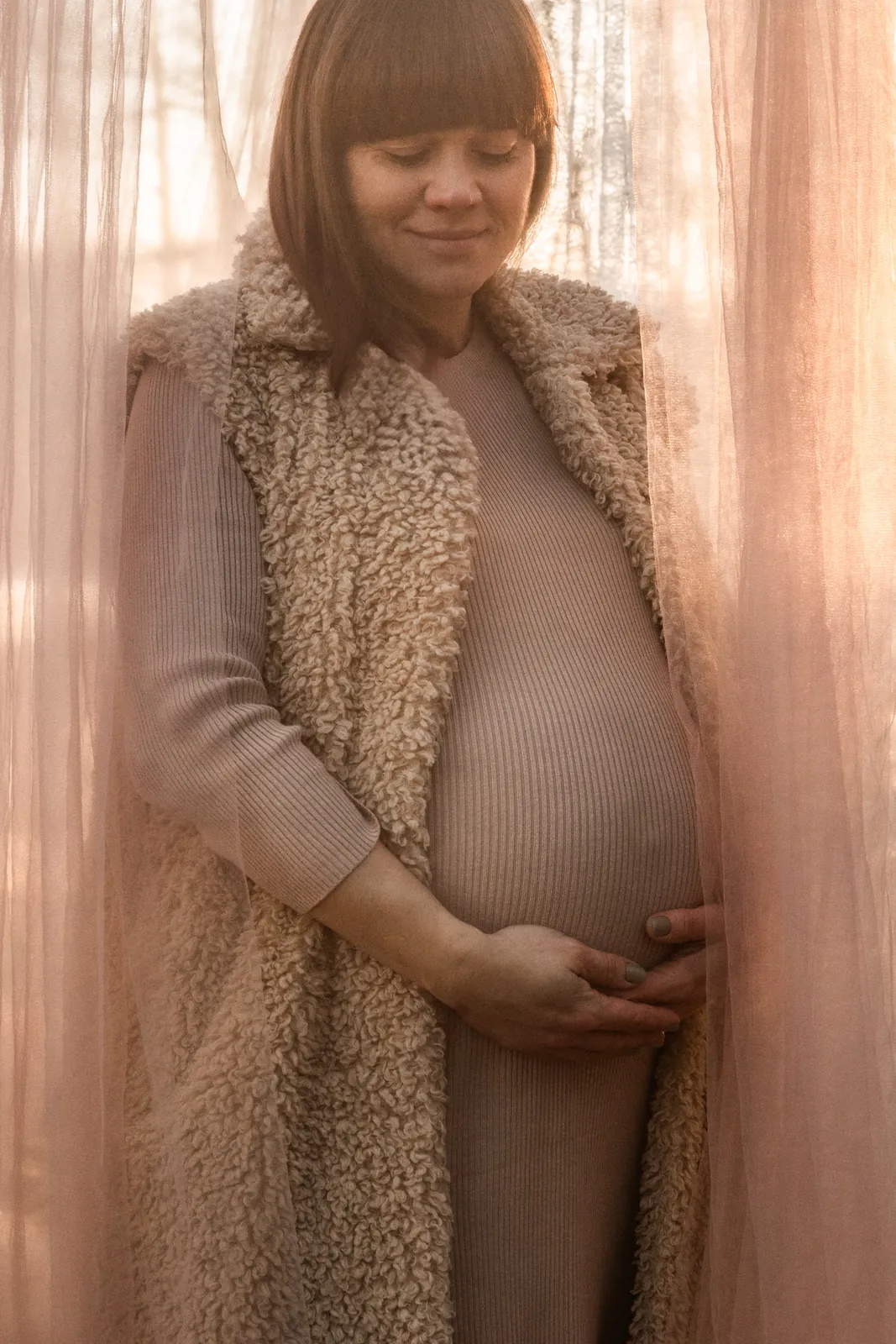 Portret przyszłej mamy otulonej delikatnym ozdobnym tiulem podczas sesji ciążowej w lesie