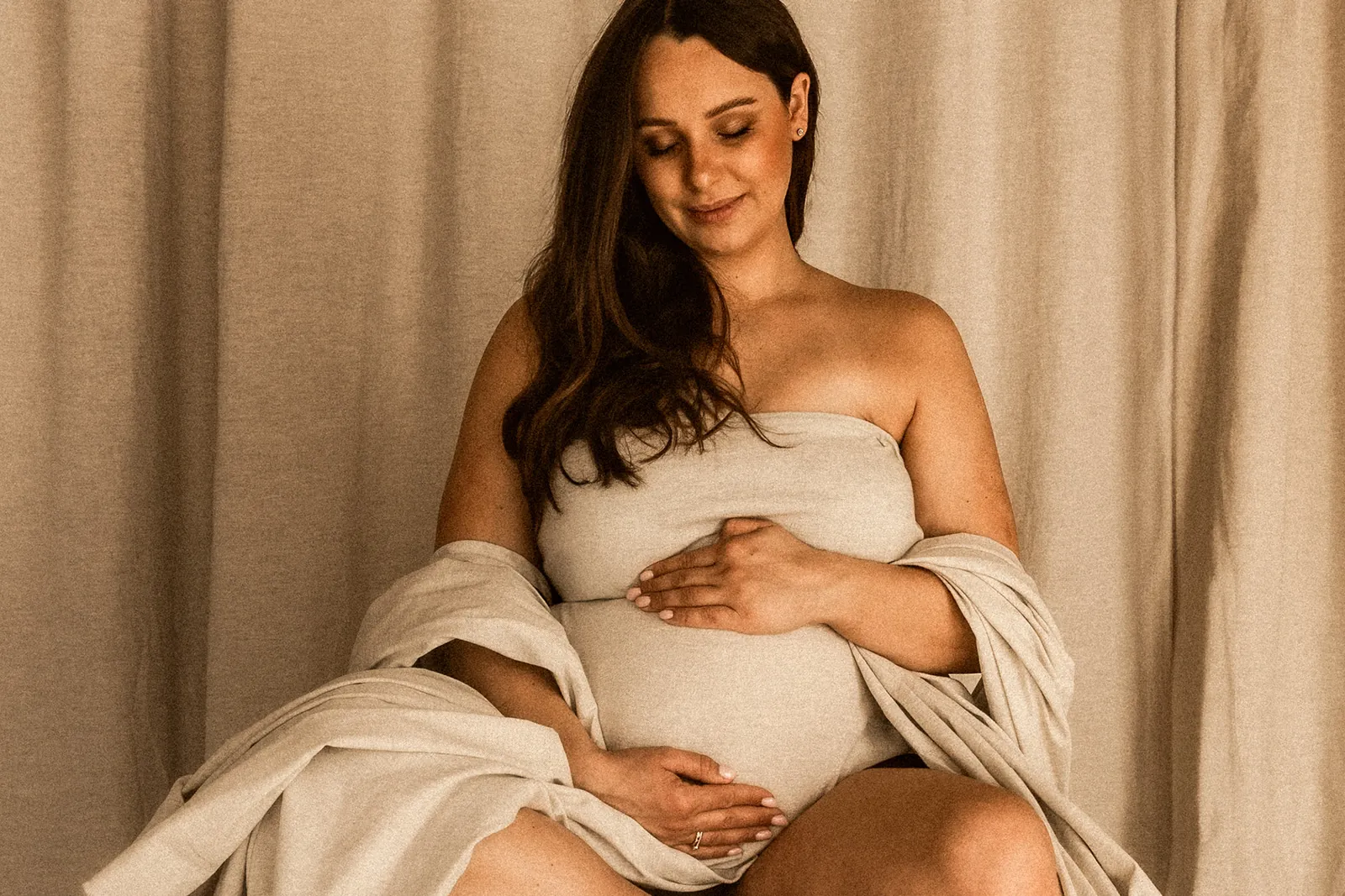 Bliski kadr przyszłej mamy w subtelnej stylizacji studyjnej i z delikatnym uśmiechem