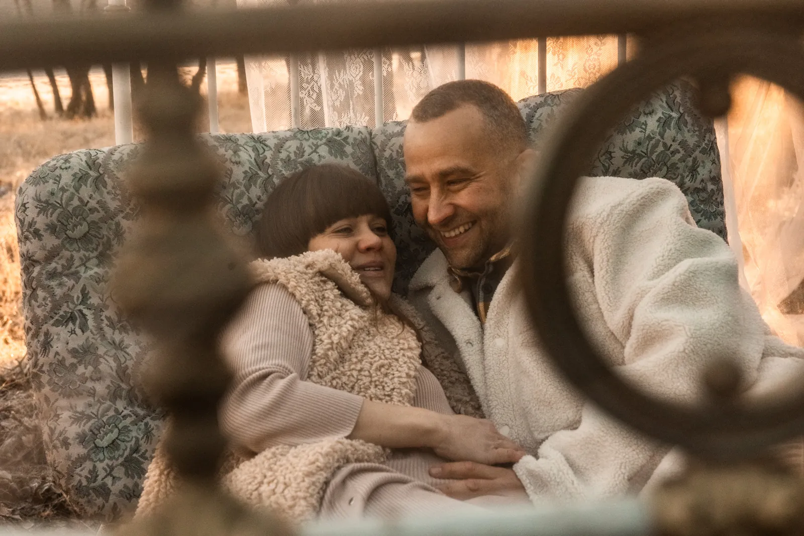 Para zakochanych przyszłych rodziców leży na łóżku przytulona do siebie podczas sesji brzuszkowej w plenerze