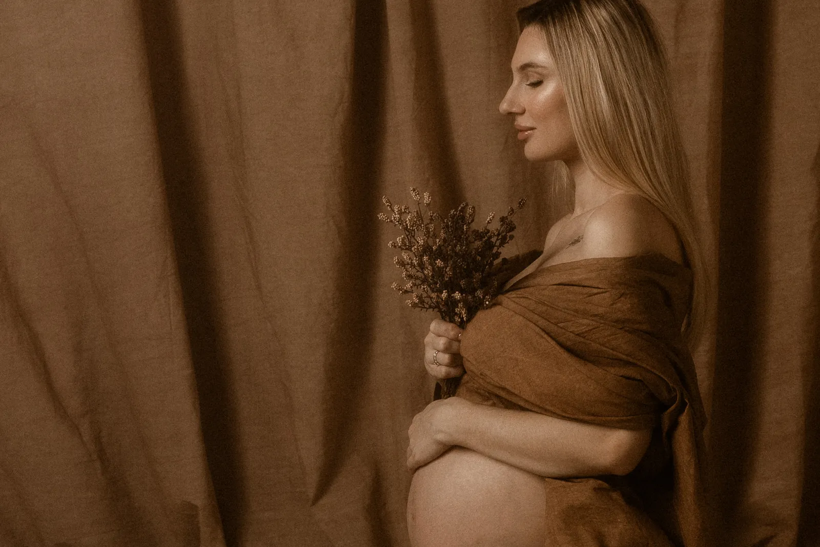 Artystyczne zdjęcie kobiety w ciąży na ciemnym tle w studiu. Przyszła mama z zamkniętymi oczami, owinięta w subtelną tkaninę.