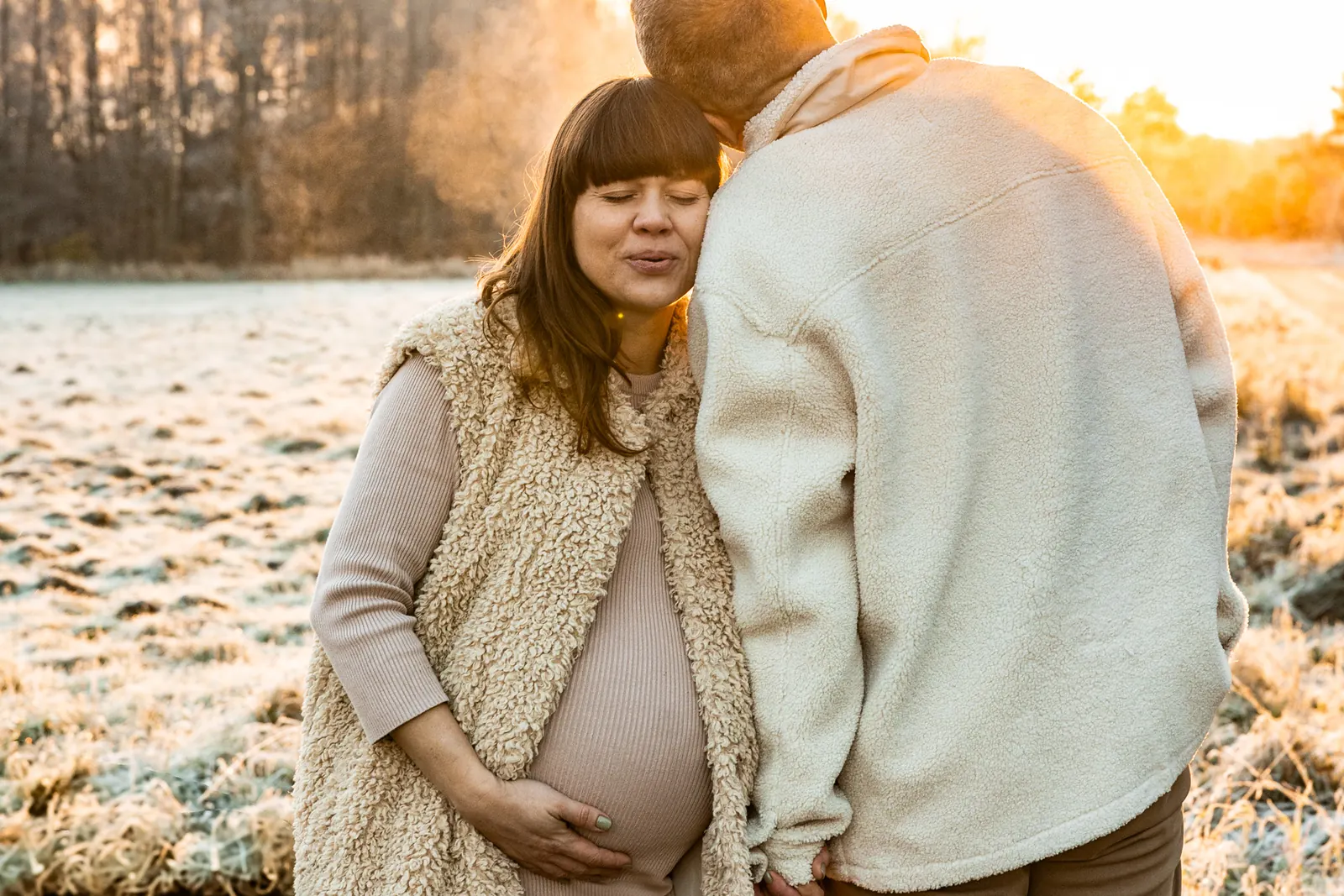 Naturalna fotografia ciążowa w plenerze – portret przyszłej pary trzymającej się za ręce. W tle łąka, las i naturalne światło.