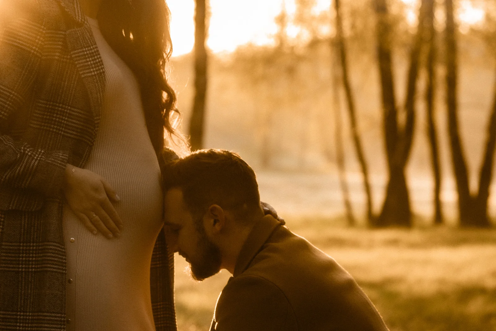 Partner delikatnie dotyka głową brzuch kobiety, w tle las i łąki