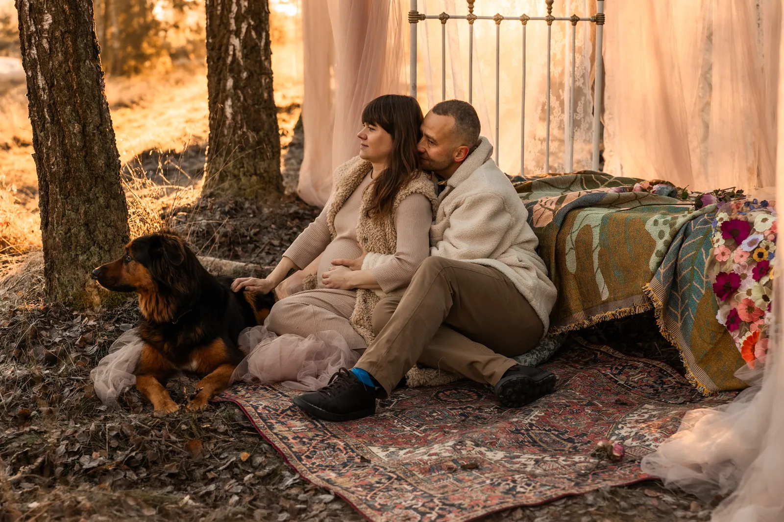 Romantyczna sesja ciążowa kobiety i mężczyzny w towarzystwie psa. W tle rekwizyty do sesji zdjęciowej w plenerze.