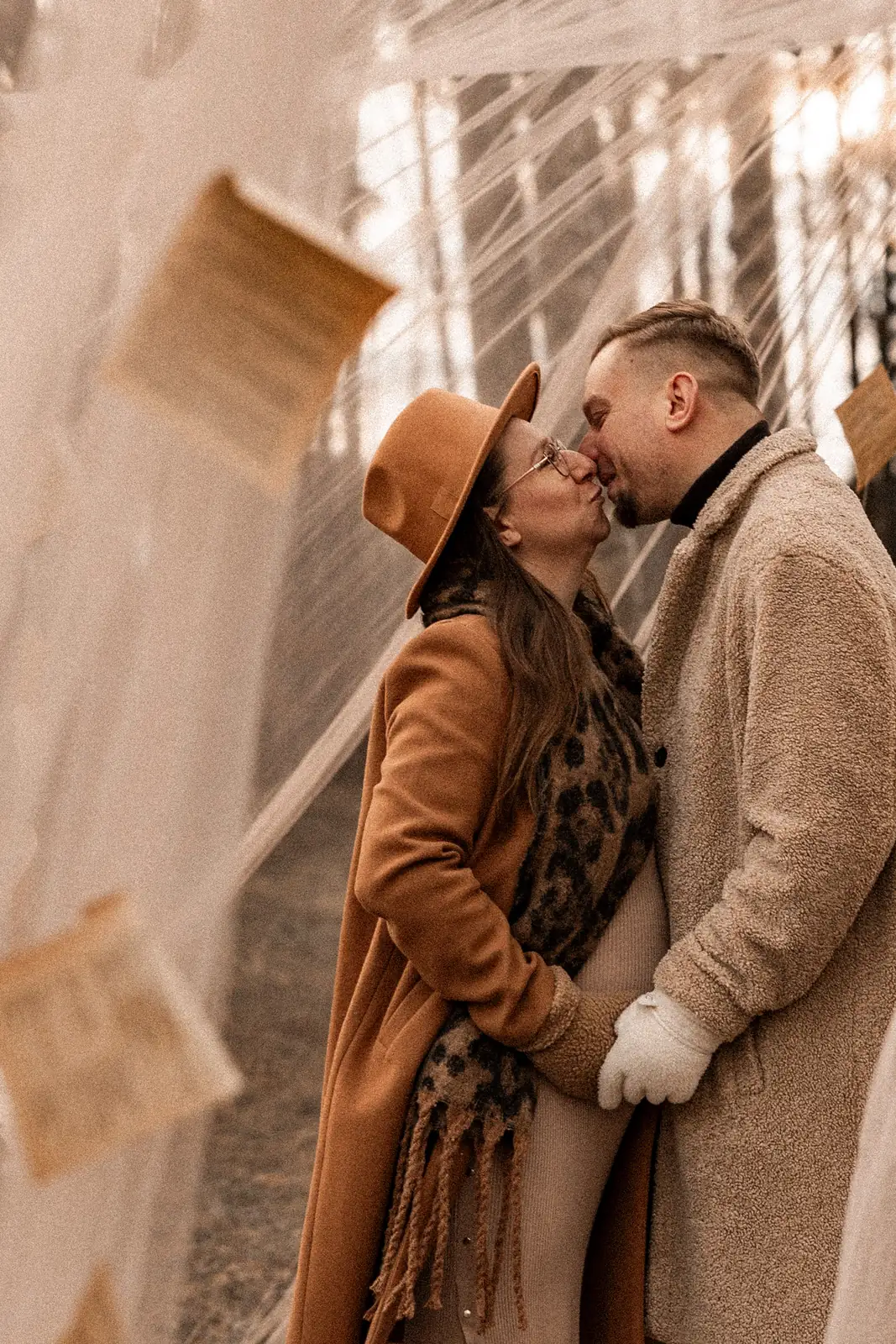 Sesja ciążowa – klasyczny portret przyszłych rodziców trzymających się za ręce. W tle powiewają subtelne dekoracje na wietrzę.