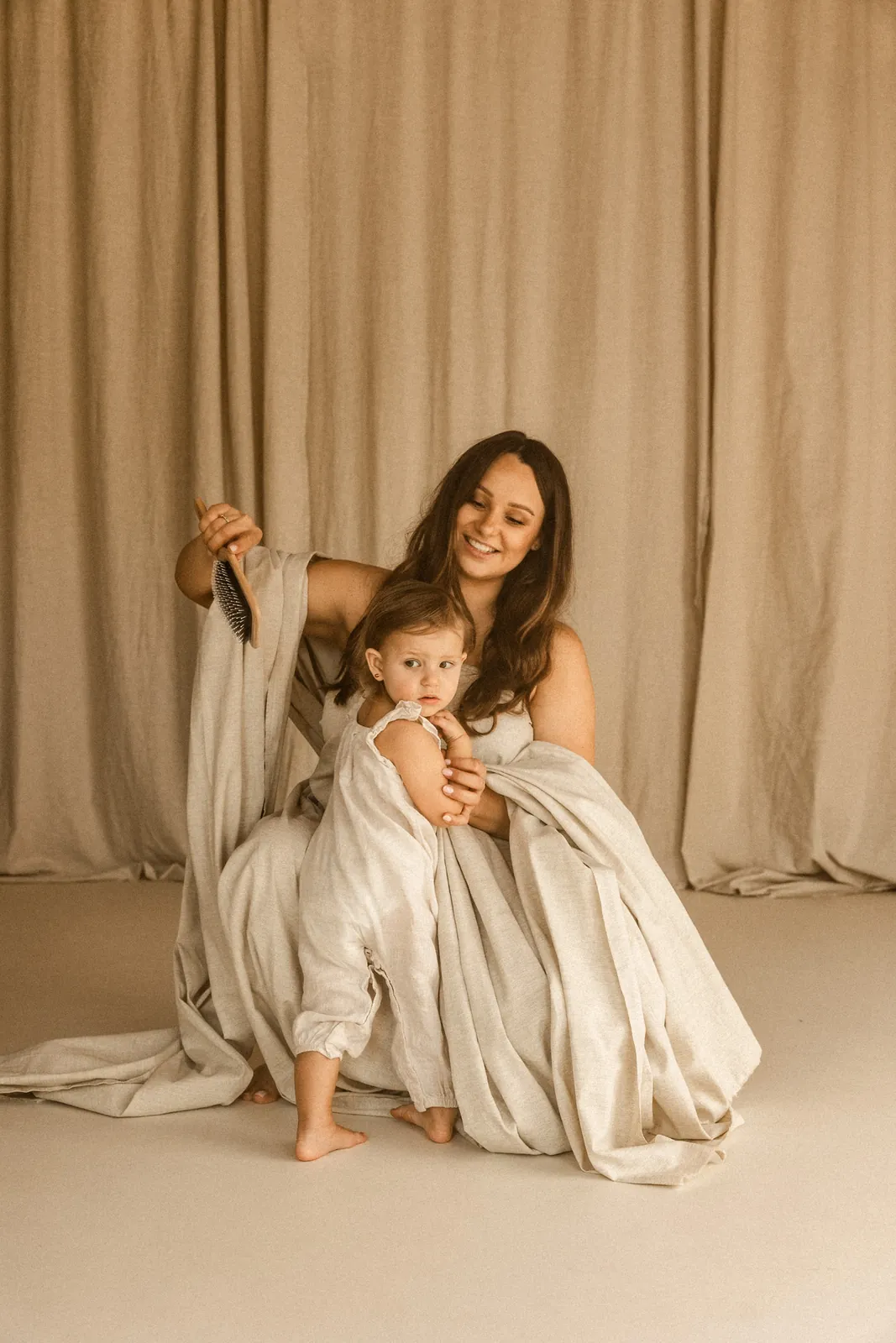 Przyszła mama czesze włosy swojej starszej córeczki podczas sesji ciążowej w stylu filmowym w studiu w Poznaniu.