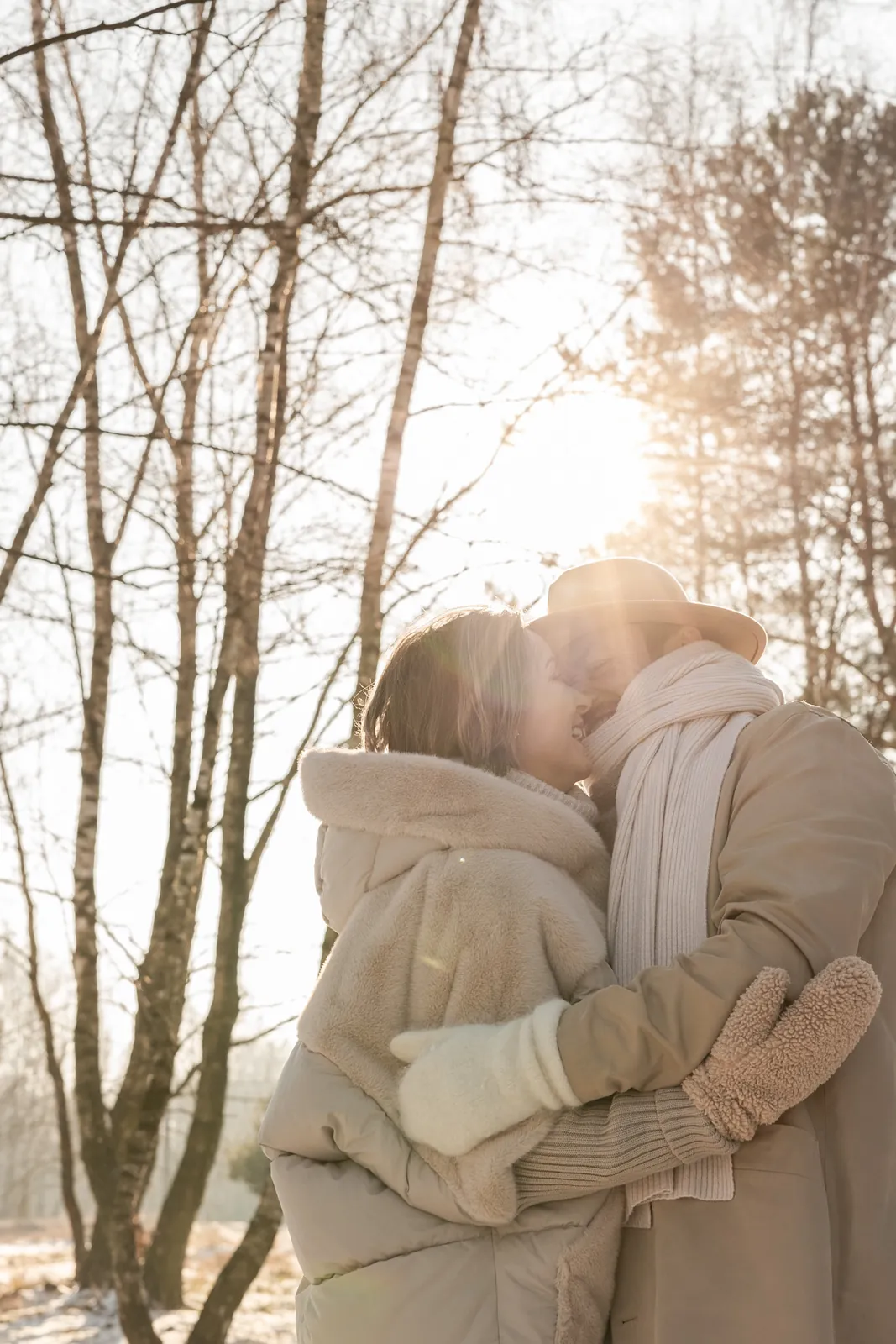 Para przytulona do siebie podczas plenerowej sesji zimowej w lesie, w tle drzewa, śnieg i wschód słońca