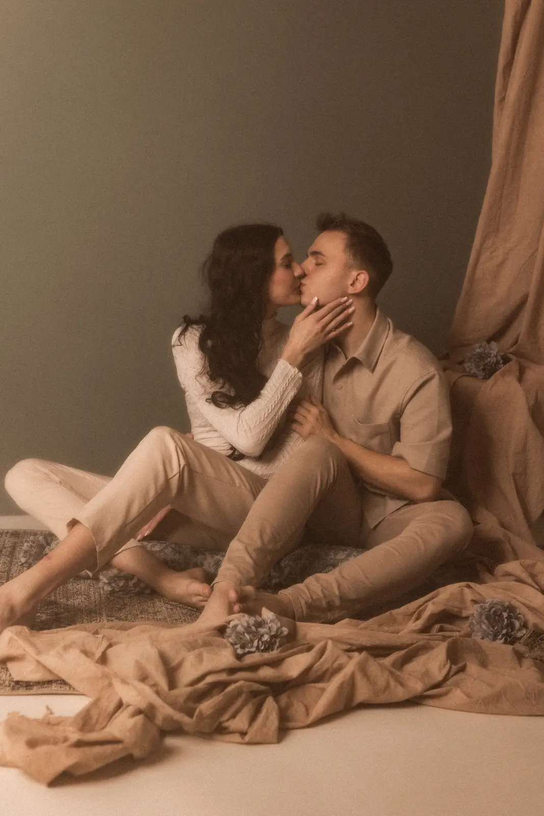 Portret pary podczas subtelnego pocałunku, w tle autorska aranżacja z materiałów i kwiatów