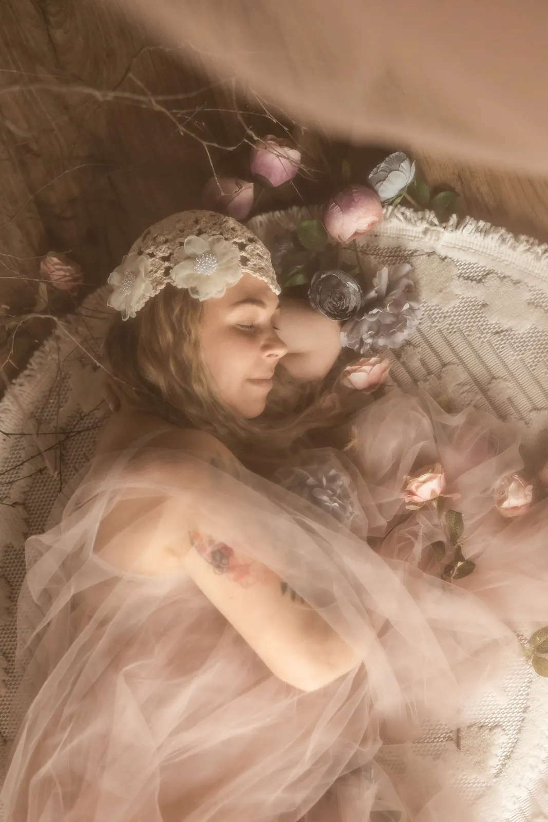 Buduarowa sesja kobieca. Kobieta z tatuażem okryta tiulem i kwiatami.