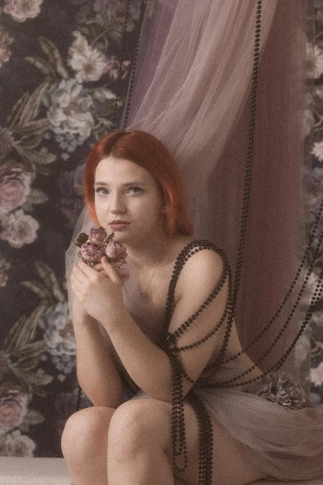 Sesja kobieca w studiu, subtelna sensualna atmosfera, Kobieta owinięta w delikatny materiał, trzyma kwiat w rękach.