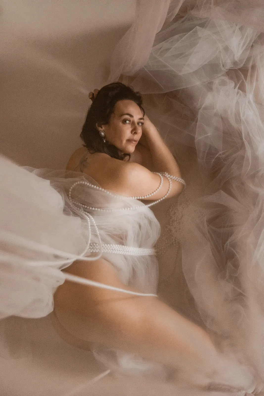 Sensualny portret kobiecy w studio. Kobieta otulona delikatnym materiałem i koralami.