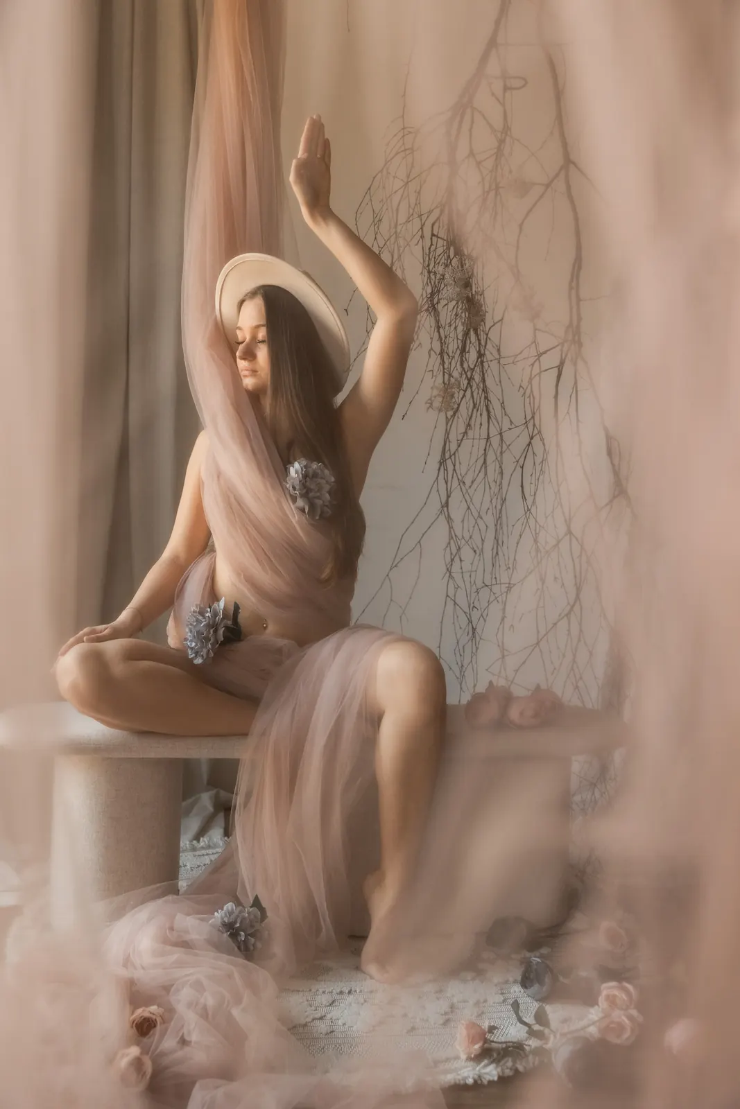 Zmysłowa sesja kobieca w studio w Poznaniu. Kobieta w kapeluszu otulona tiulami, w tle ozdoby natury.