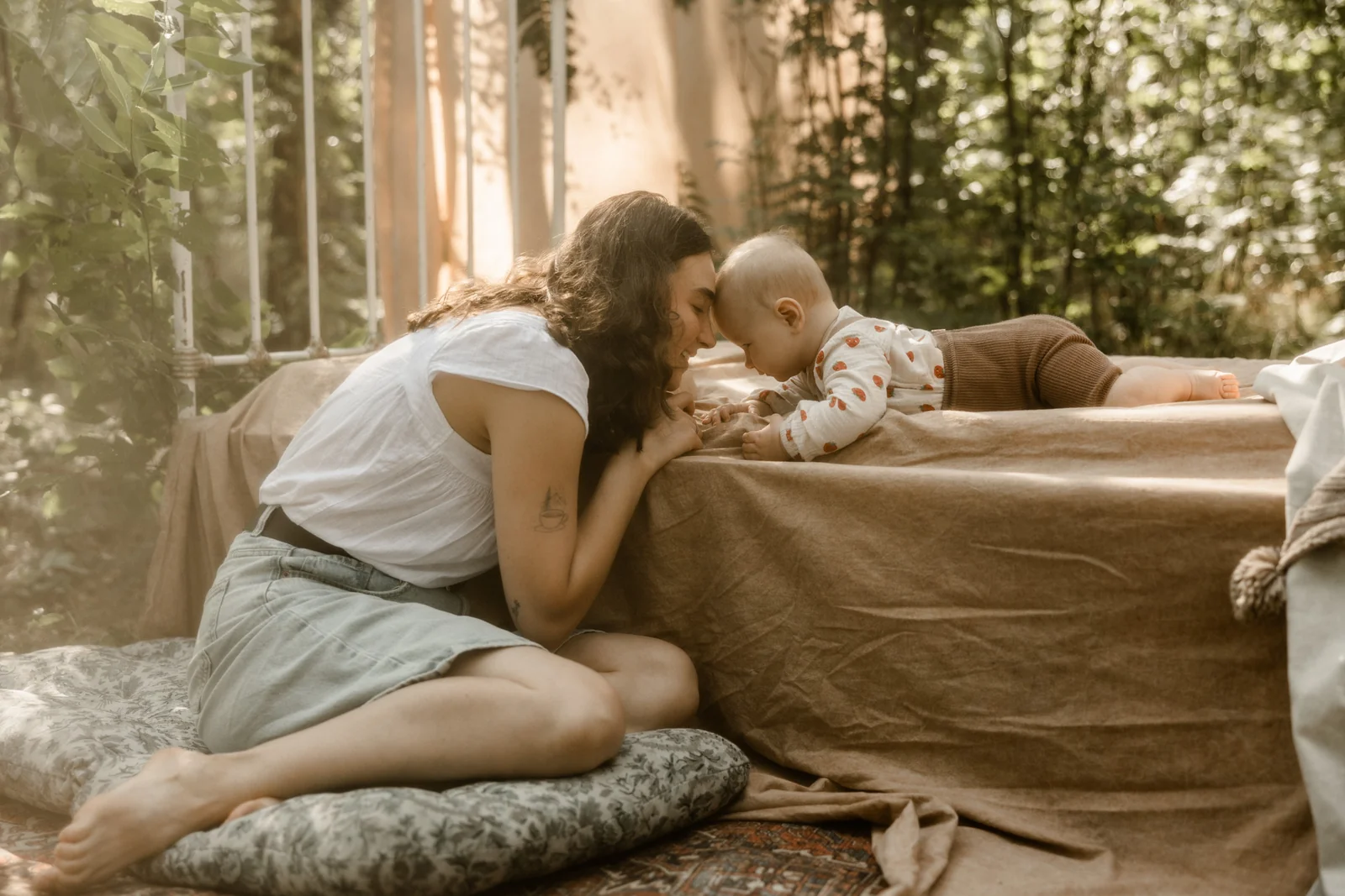 Mama kucająca na poduszce i stykająca czoło niemowlaka leżącego na leśnym łóżku