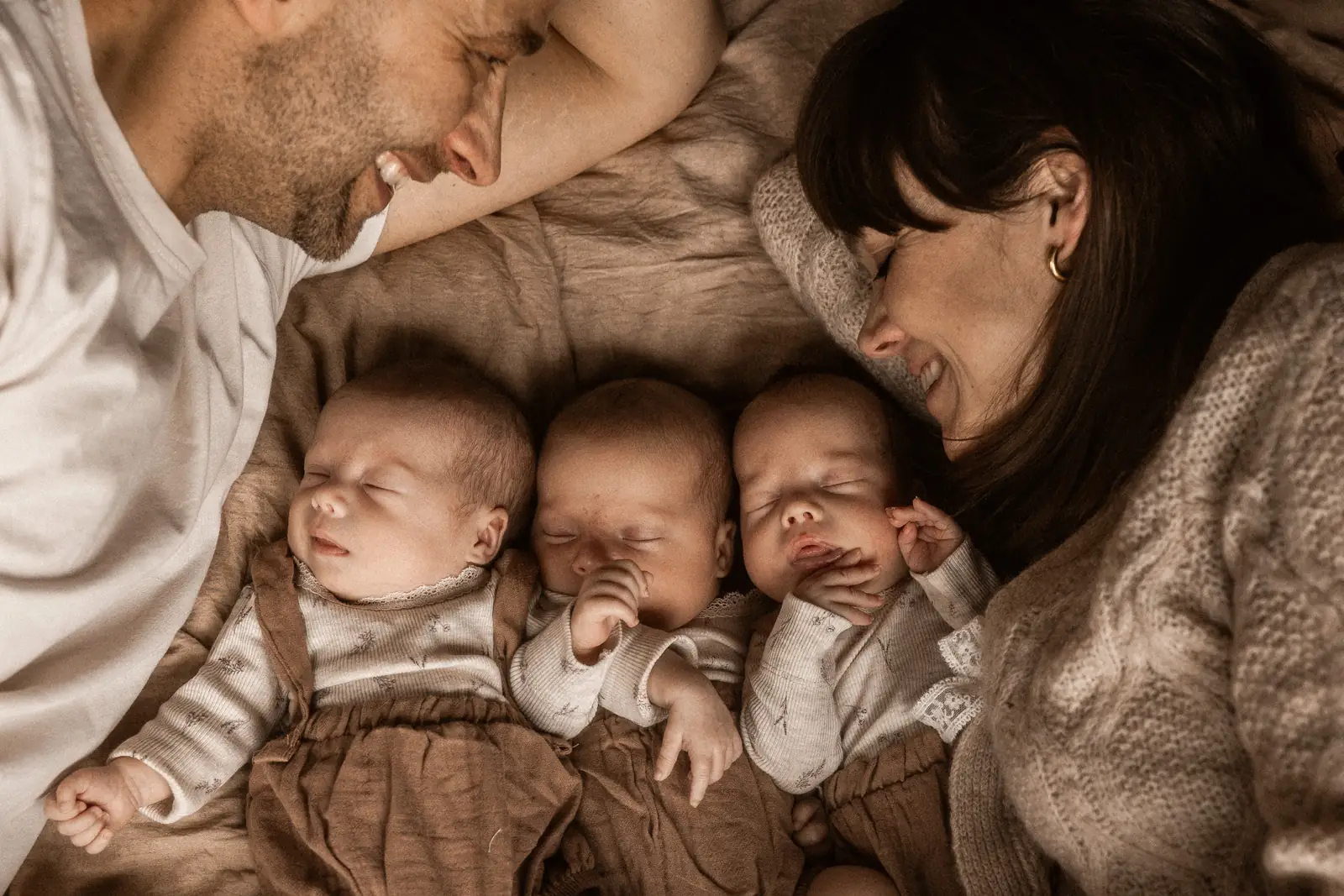 Uśmiechnięci szczęśliwi rodzice razem z małymi córeczkami podczas naturalnym sesji noworodkowej w domu