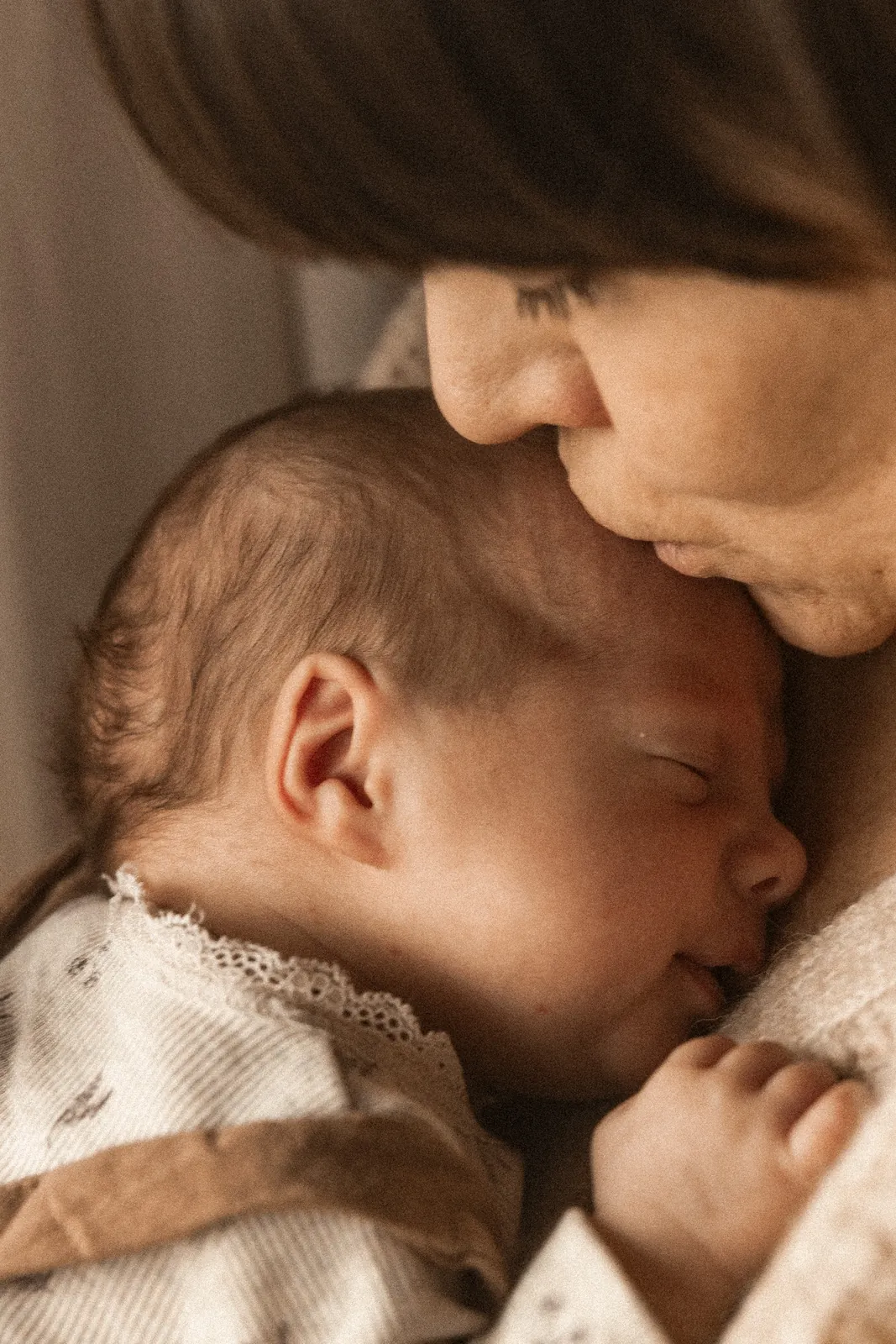 Bliski portret mamy całującej czule główkę śpiącego dziecka podczas domowej sesji noworodkowej