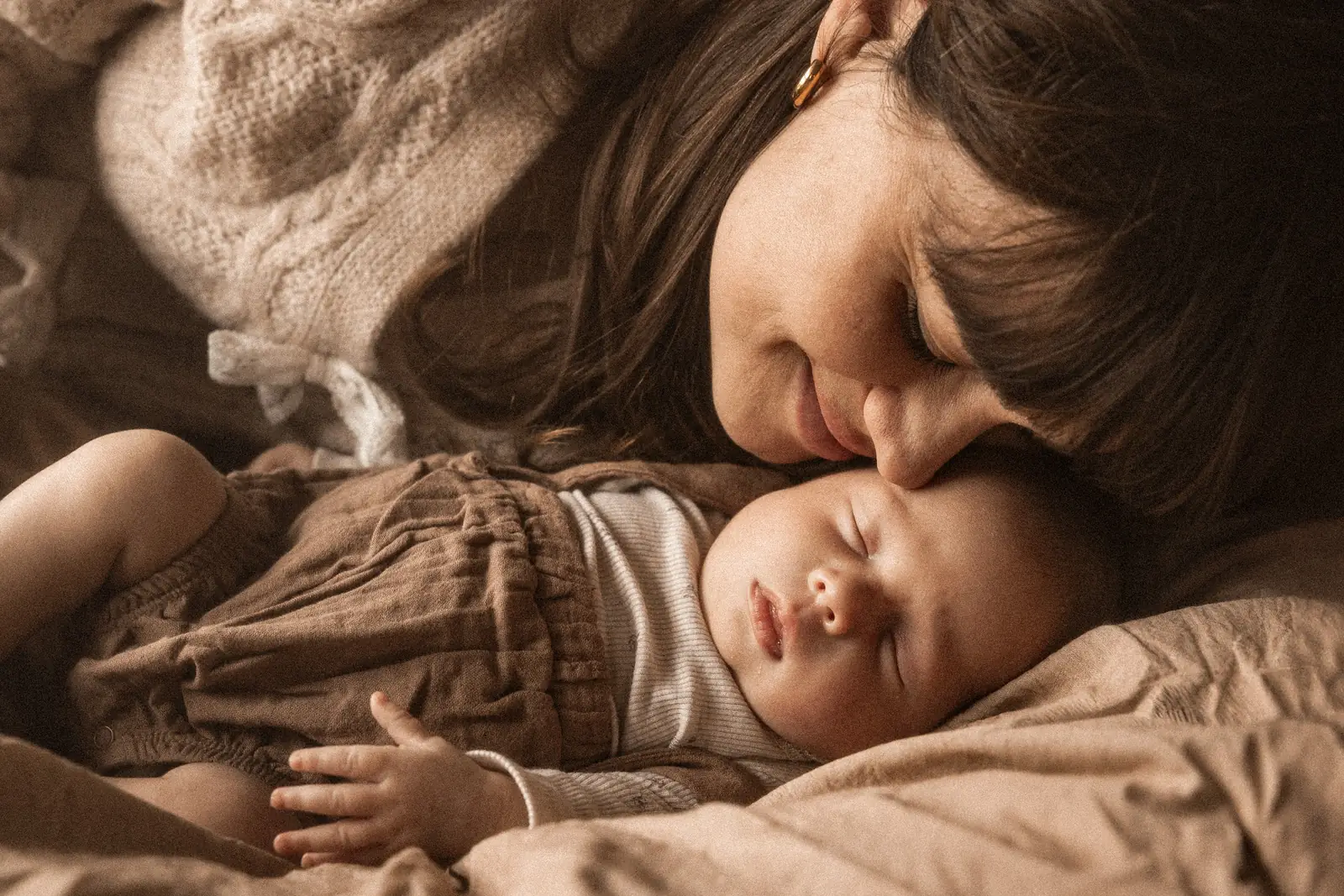 Czuły kadr mamy przytulającej twarzą twarz śpiącej córeczki podczas sesji noworodkowej w domu rodzinnym
