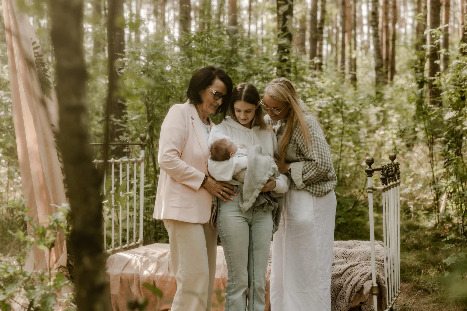 Trzy kobiety przytulone do noworodka - mama, babcia i prababcia podczas naturalnej sesji w plenerze
