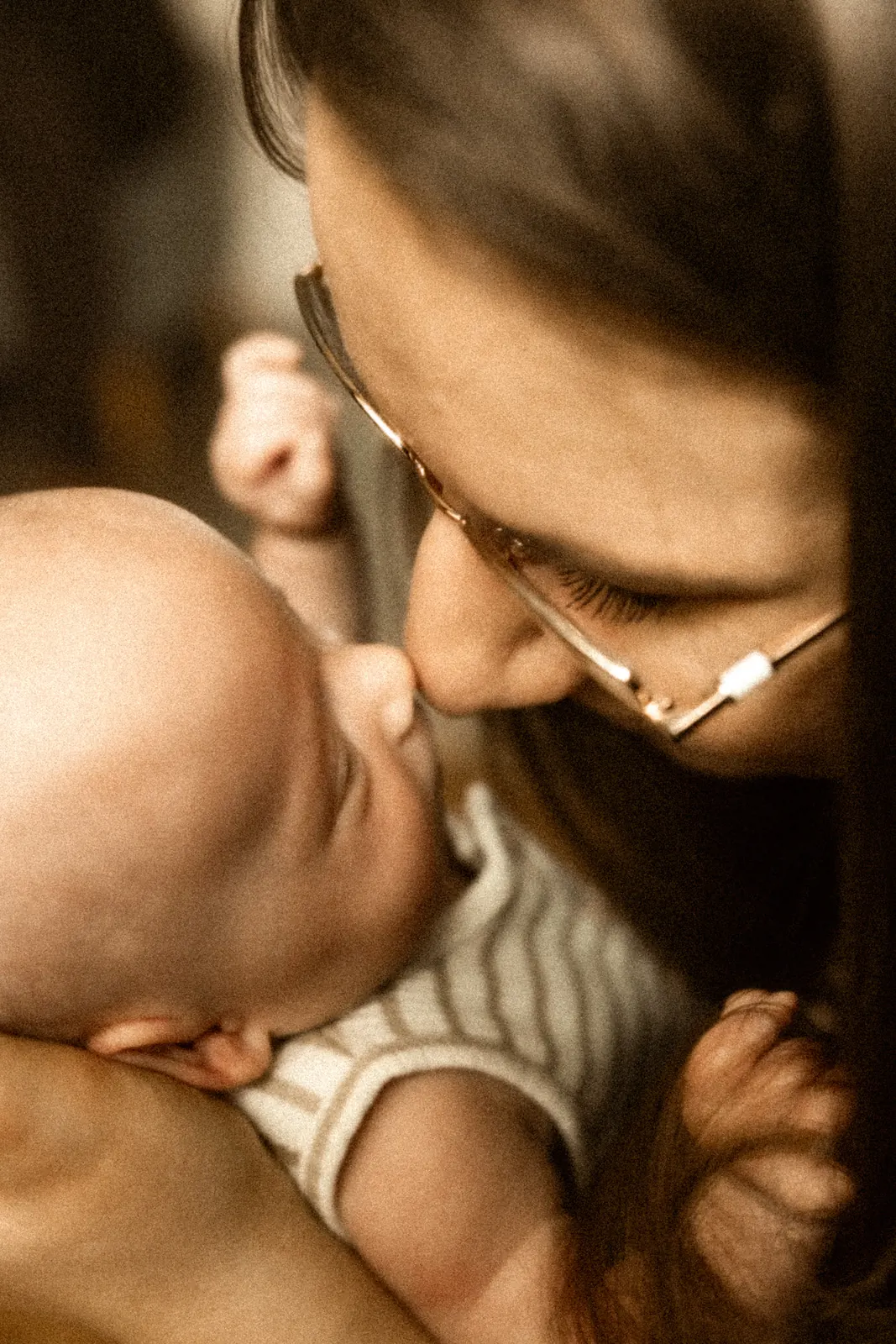 Czuły moment mamy przytulającej dziecko i delikatnie muskającej noskiem nosek noworodka uchwyconay podczas sesji lifestyle