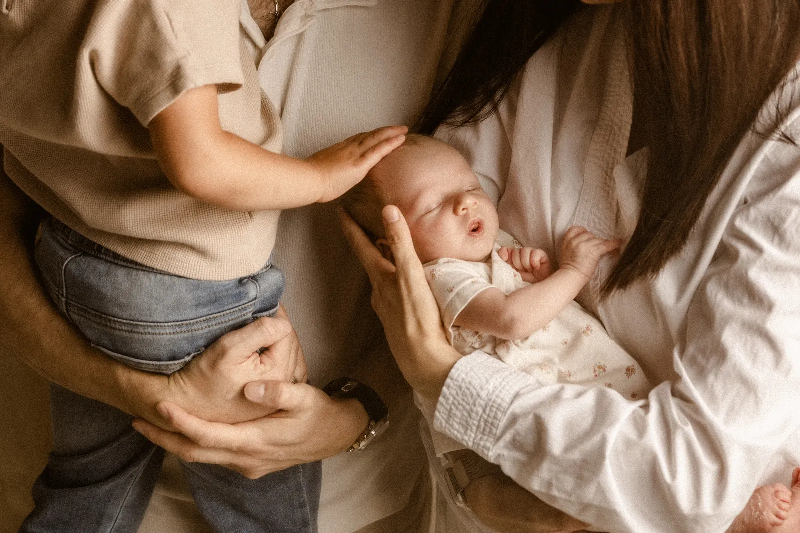 Mama otula maluszka, a starsze rodzeństwo dotyka delikatnie główki podczas sesji noworodkowej w studiu