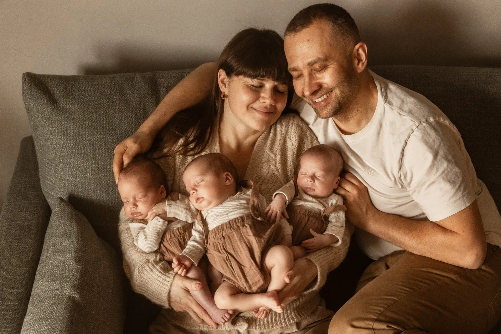 Trojaczki śpiące w ramionach mamy. Tata czule przytula mamę.