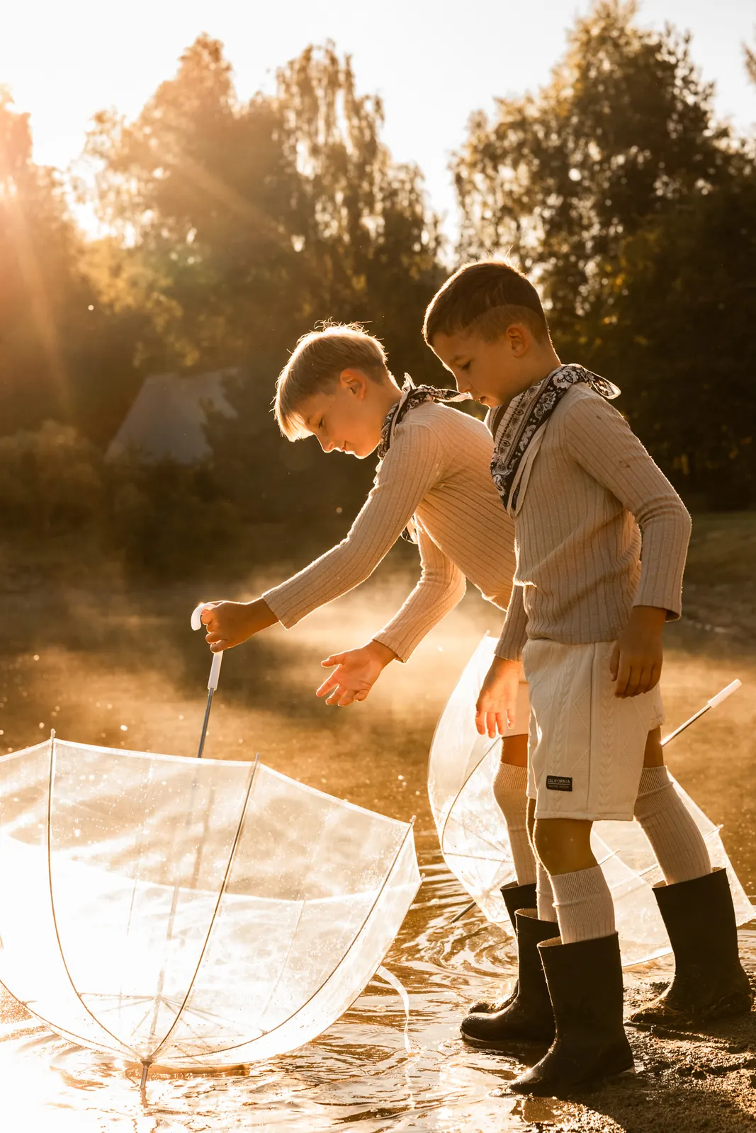 Dwóch chłopców bawi się parasolami nad jeziorem w porannym świetle
