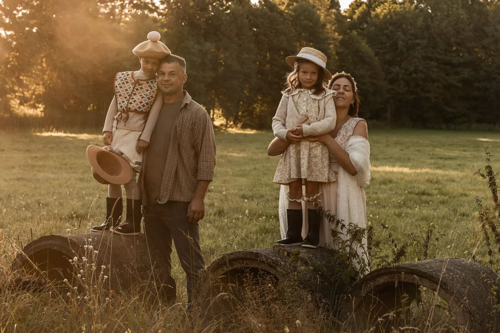Mama, tata, córka i syn w wiejskiej scenerii na sesji zdjęciowej. W tle łąka i drzewa.