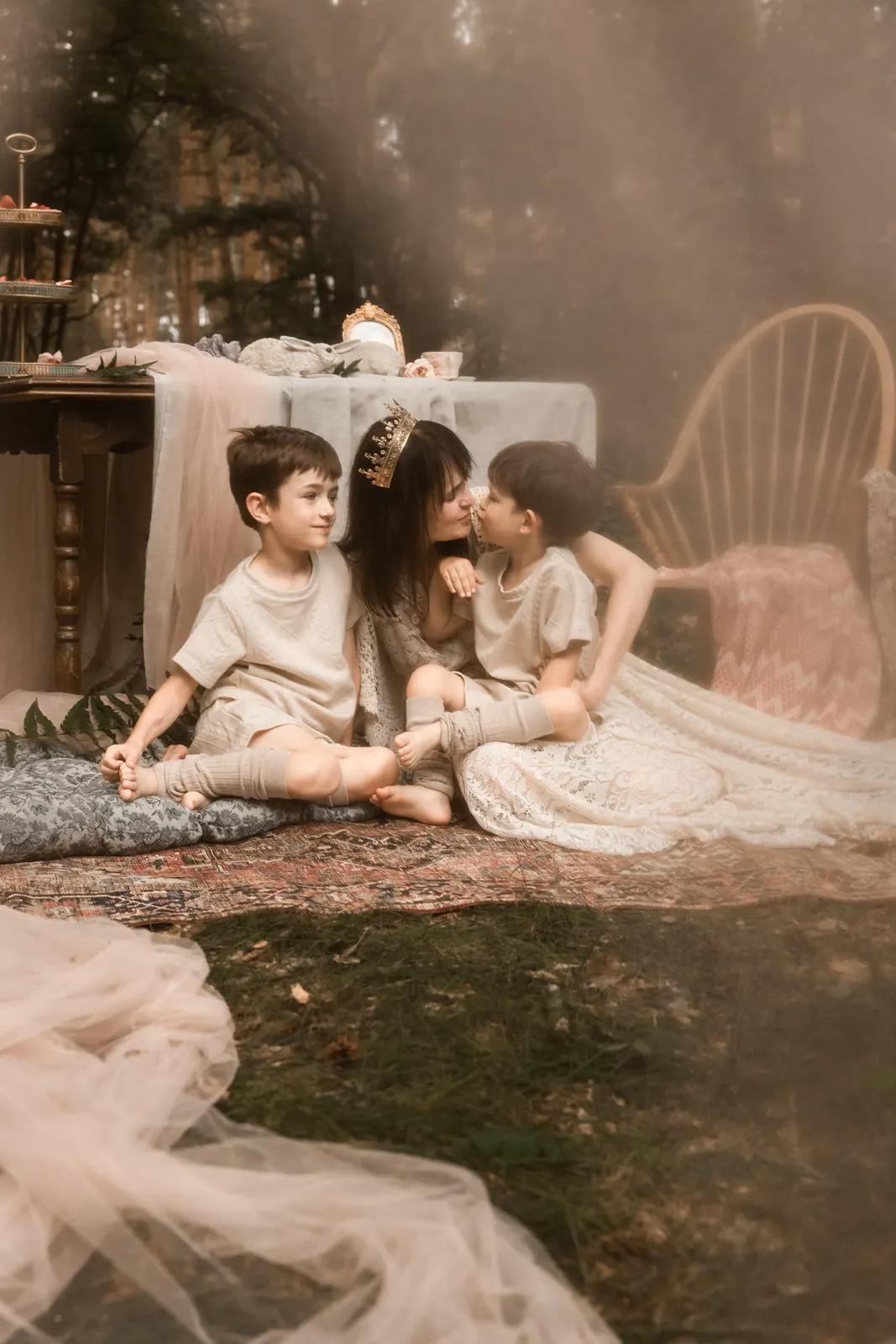 Mama przytulająca dzieci w plenerze, stylizowana przestrzeń z dodatkami, las w tle