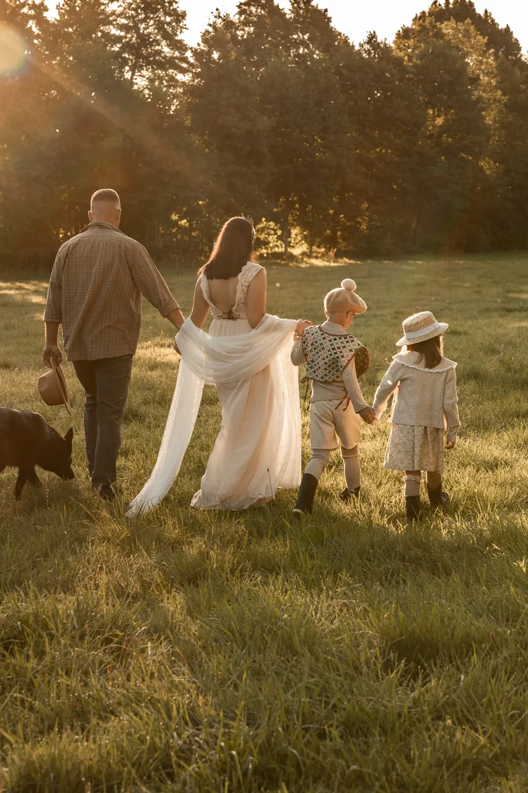 Rodzice z dziećmi trzymający się za ręce, idą przez łąkę wraz z swoim psem, w naturalnym świetle