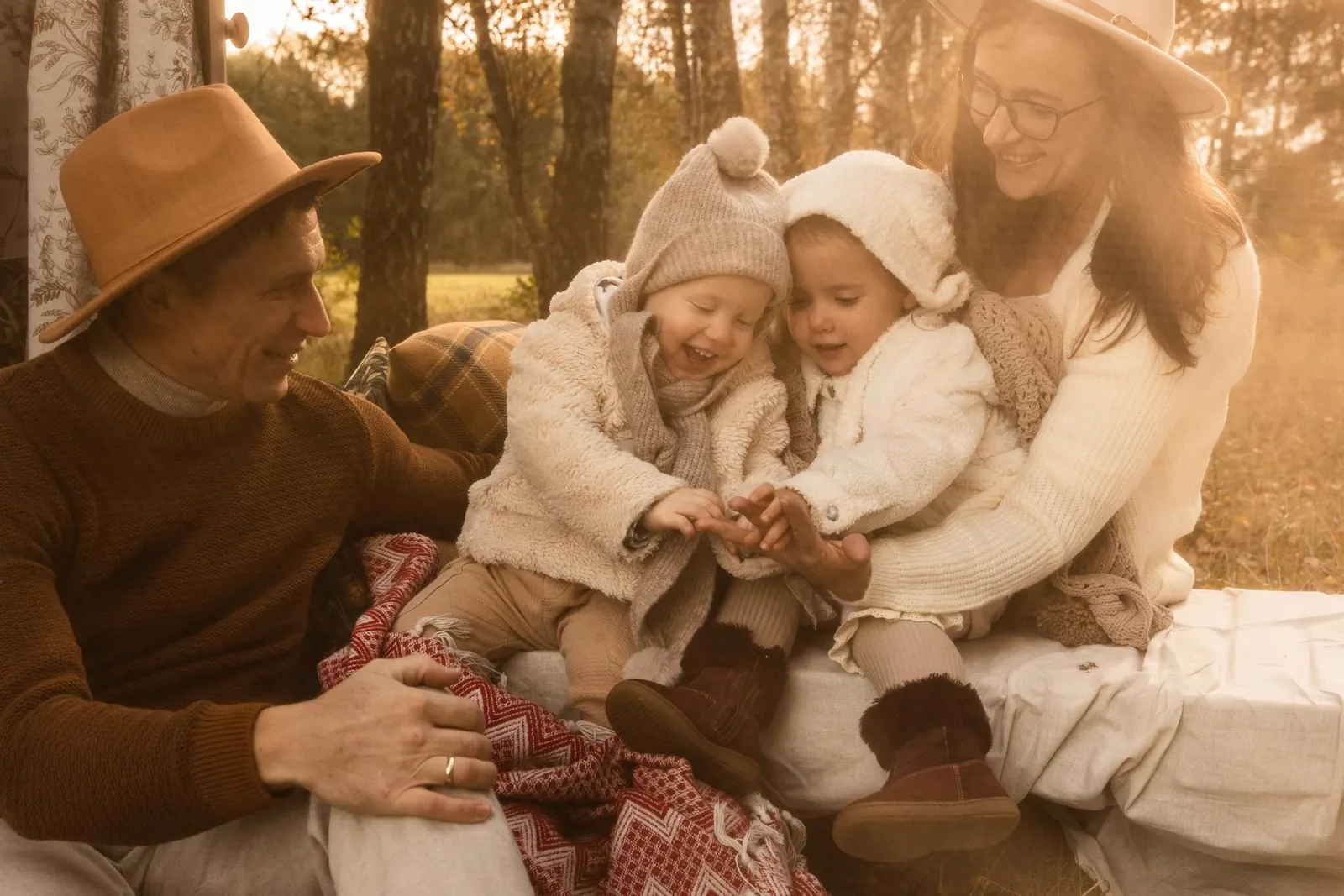 Rodzice z dziećmi w leśnej scenerii podczas rodzinnej sesji plenerowej. W tle drzewa i wschód słońca.
