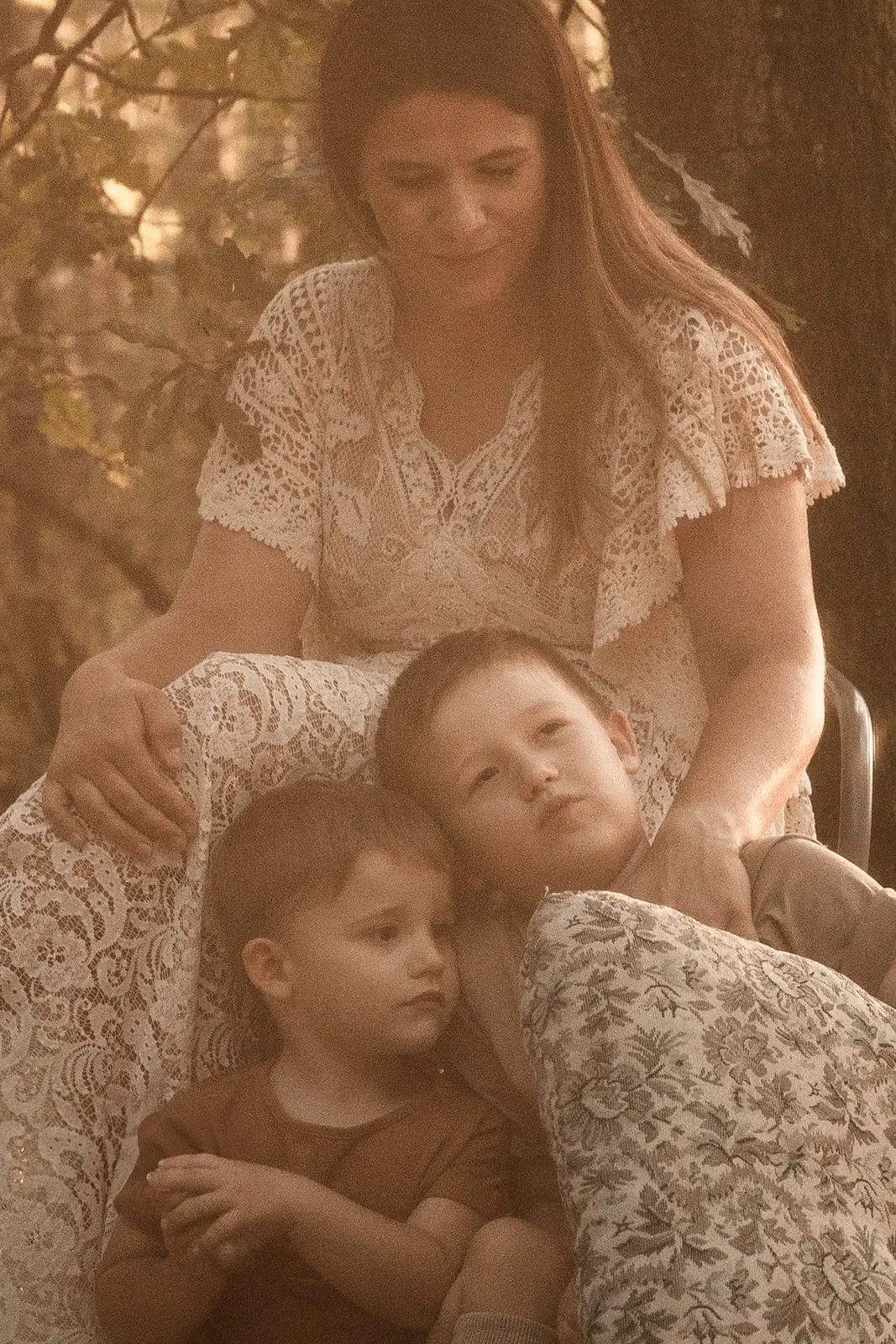 Ciepła sesja mamy z dziećmi w lesie, stylizowana aranżacja plenerowa. Mama ubrana w koronkową suknie.
