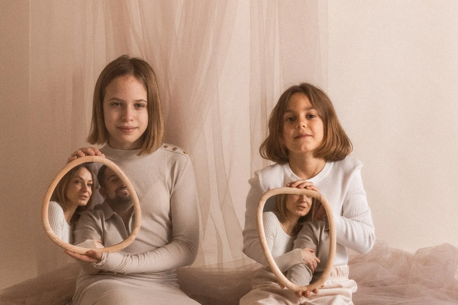 Rodzina podczas minimalistycznej sesji zdjęciowej w studiu. Dzieci trzymają lusterka w których widać odbicia rodziców.