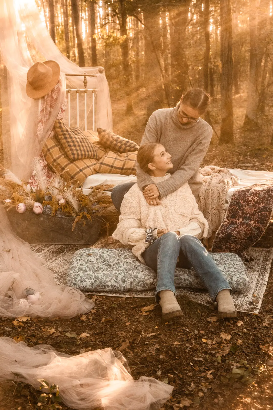 Naturalny portret mamy i córki, w tle meble użytku domowego w leśnej inscenizacji plenerowej tworzące widowisko artystyczne