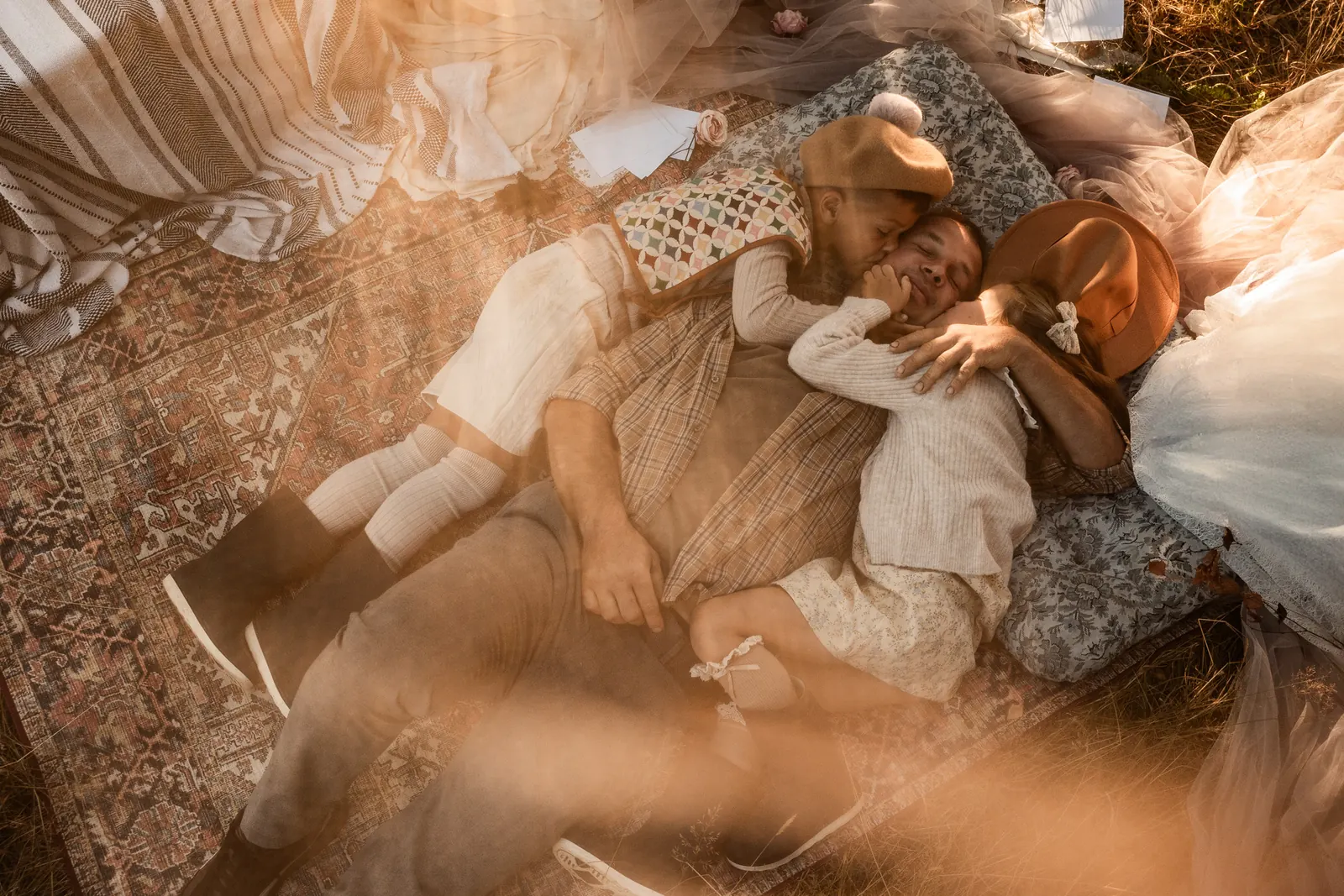 Tata z dziećmi pozujący w stylizowanej scenerii plenerowej, w tle naturalne światło wschodzącego słońca.