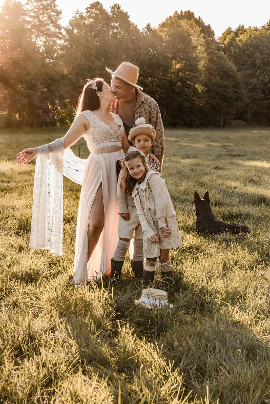 Spontaniczne chwile rodziców z dziećmi i psem podczas rodzinnej sesji w plenerze. W tle łąka, las i wschód słońca.