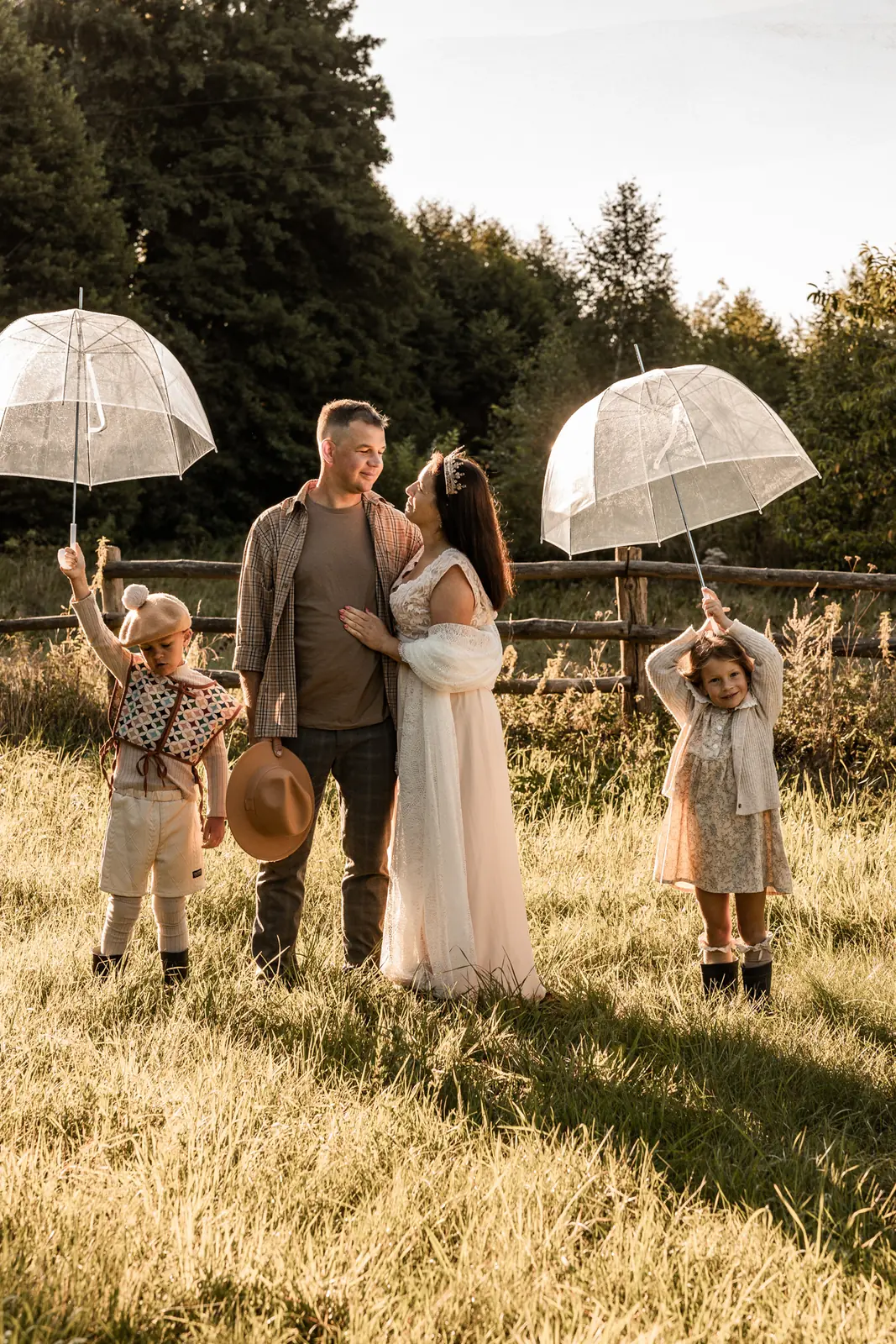 Rodzinne zdjęcie mamy, taty i dzieci na polanie podczas lifestylowej rodzinnej sesji plenerowej. Dzieci bawią się parasolami.